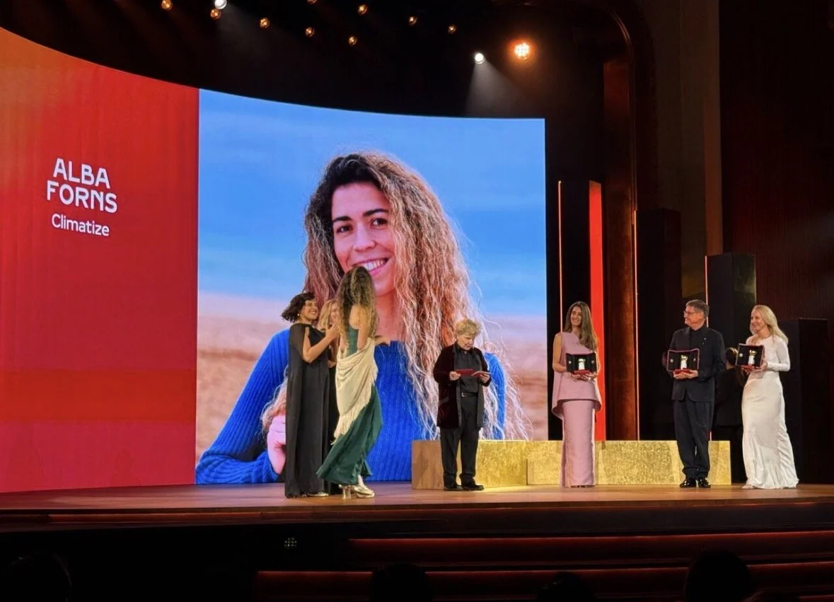 Alba walks on stage to accept her Cartier award. On the stage are 6 other people, some holding awards and some applauding