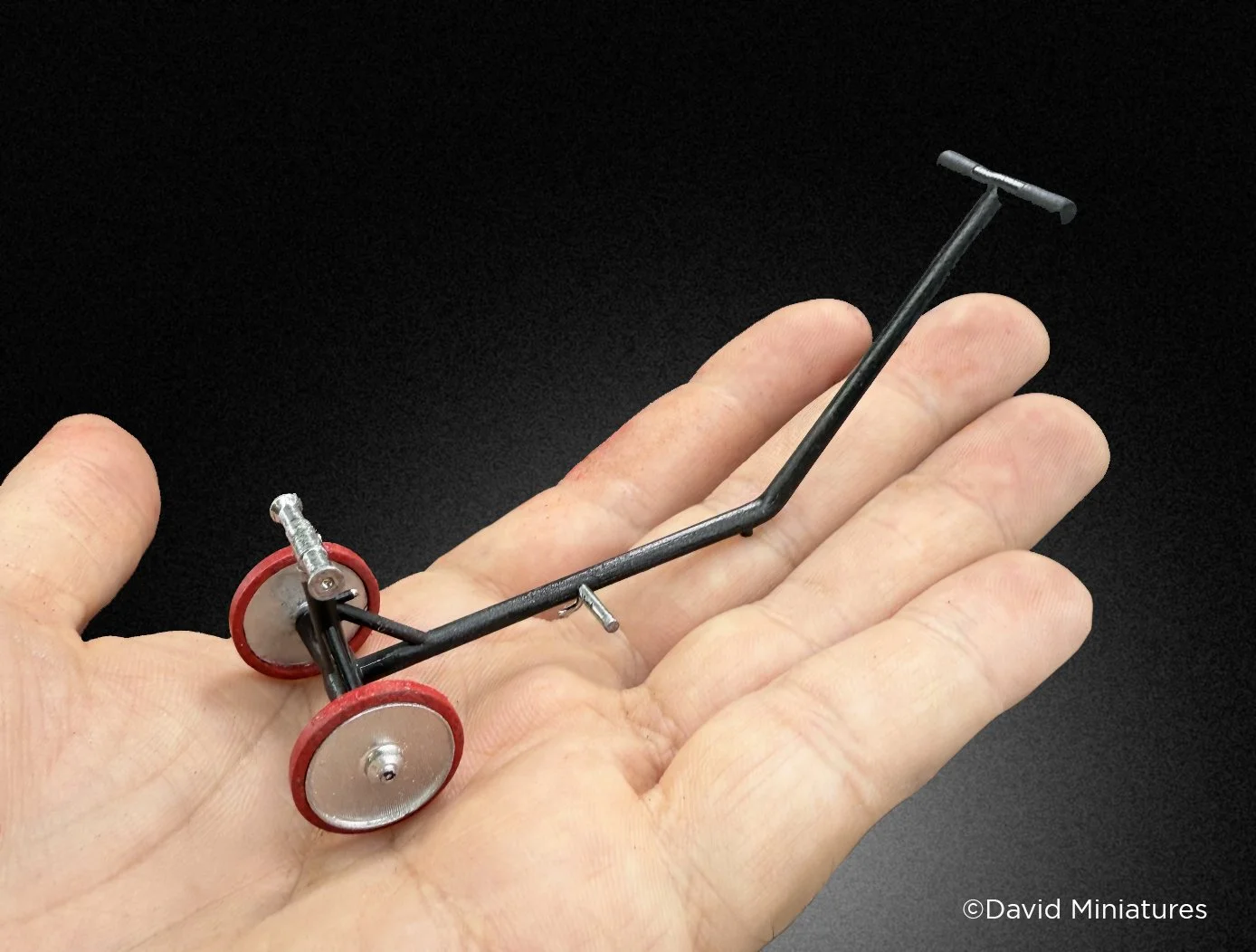 Small model vehicle with black frame, red and silver wheels, and a T-shaped handle, resting on a person's hand.