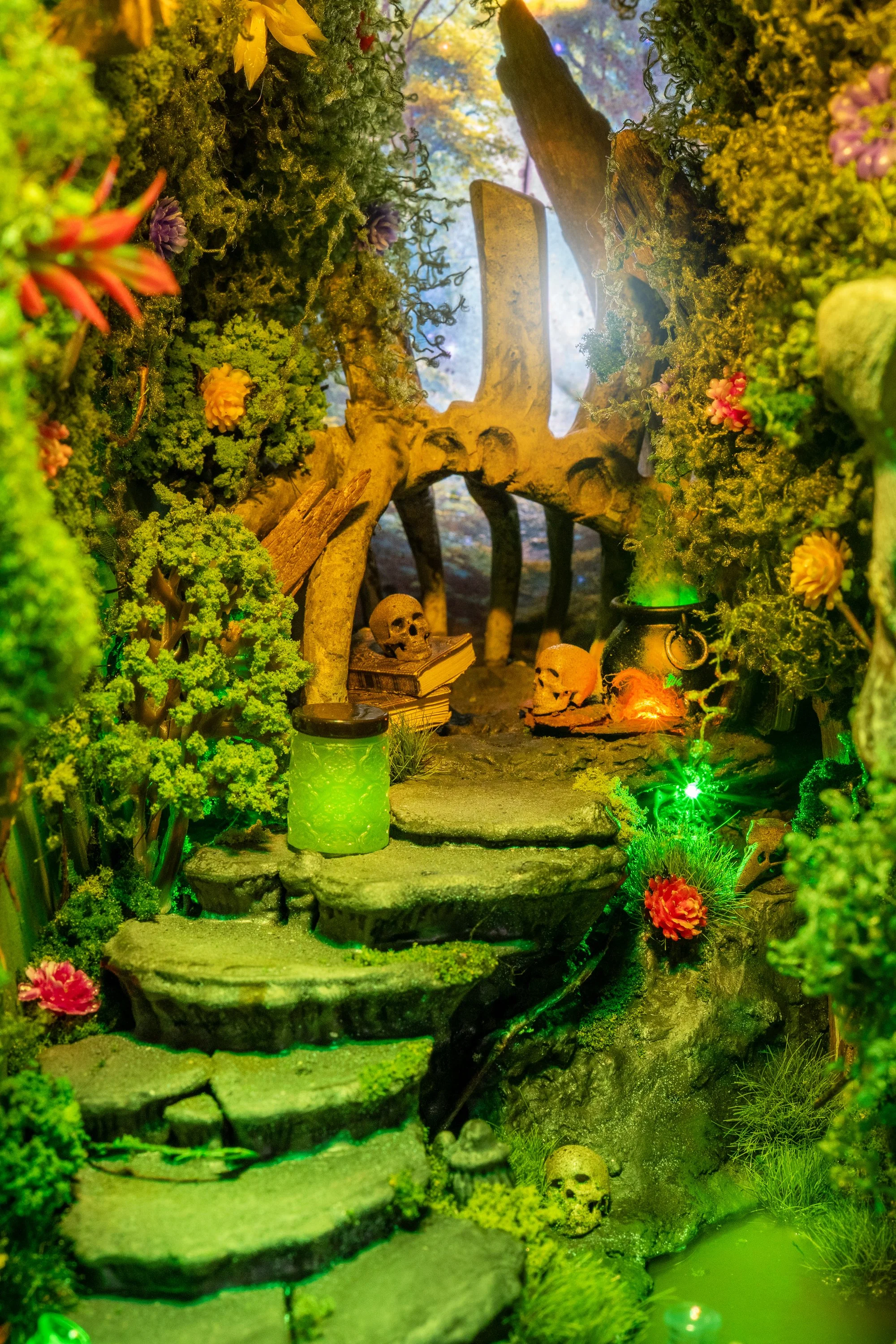 Miniature fantasy scene of a forest with moss and plants, skulls, a small waterfall, and glowing lights.