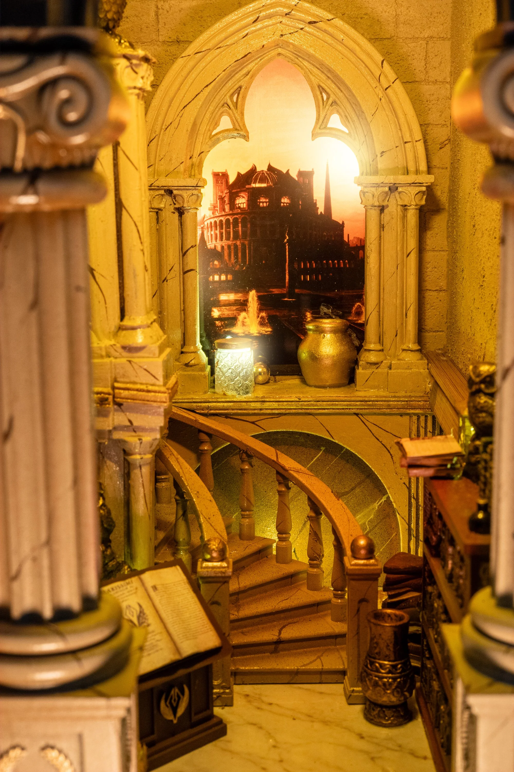 A decorative interior scene resembling a library or study, with a painted window showing a cityscape and a fountain, surrounded by ornate architectural details, books, jars, and decorative objects.
