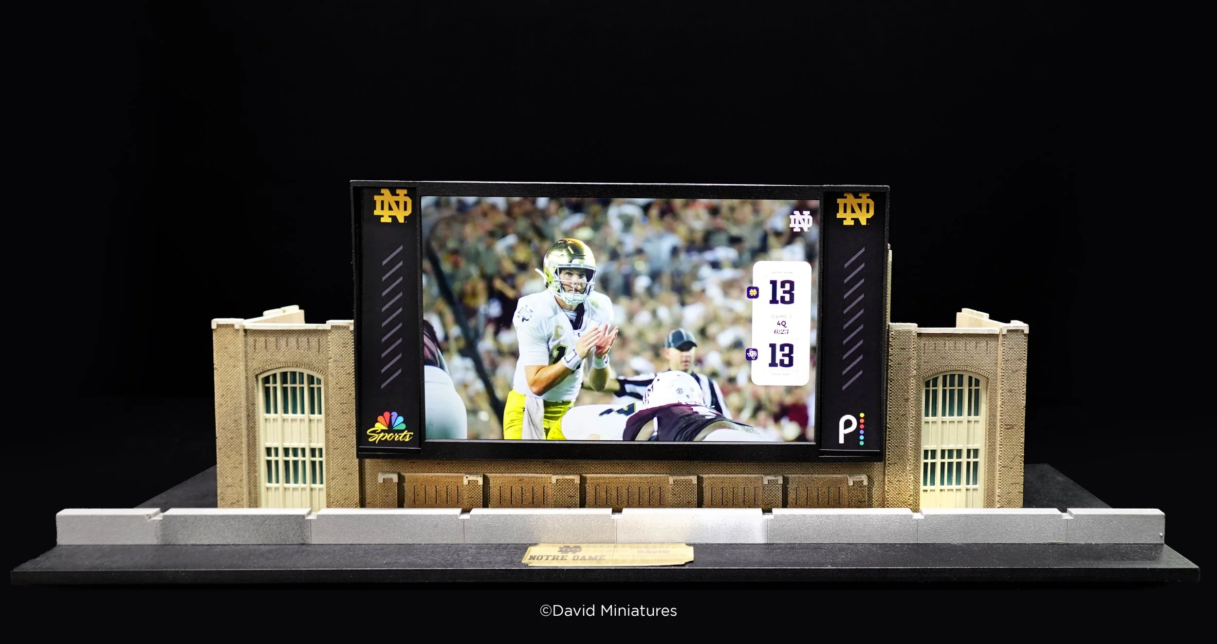 Miniature model of Notre Dame stadium with a digital scoreboard displaying a football game, featuring a quarterback and team logos.