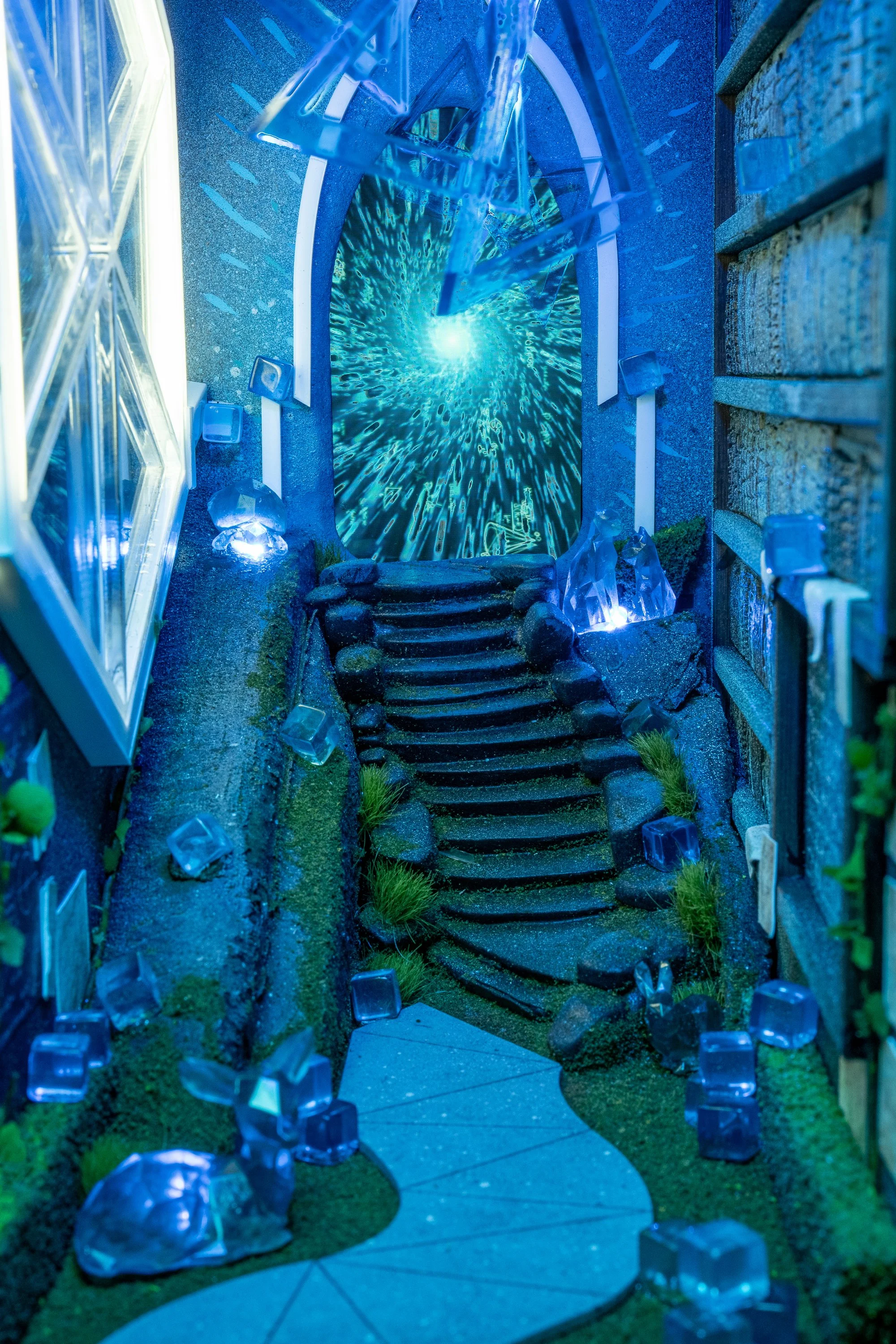 A fantasy-themed miniature diorama depicts a mystical blue portal at the end of a stone pathway, with crystal formations and glowing lights enhancing the enchanted ambiance.