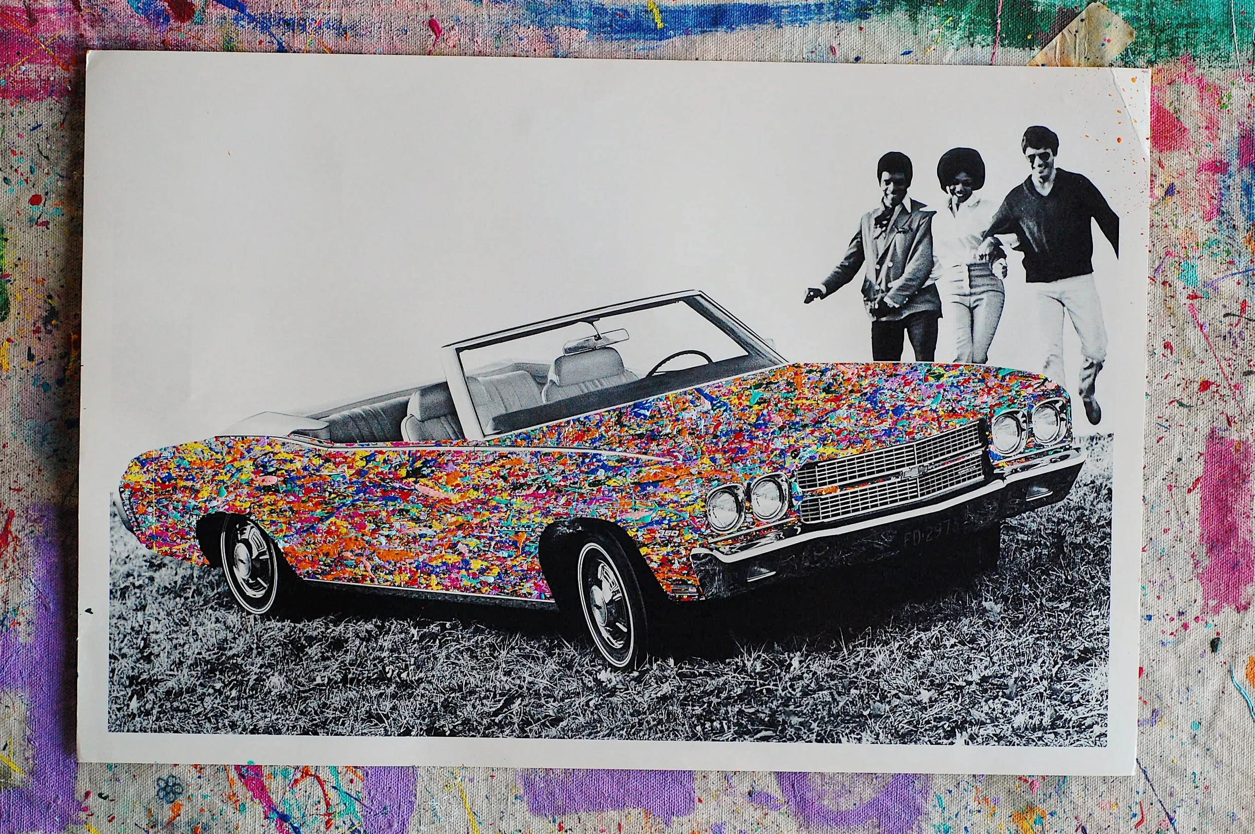 Full view of a mixed-media artwork featuring a vintage 1970 Chevy Malibu convertible with colorful paint splatter, photographed in an artist studio setting.