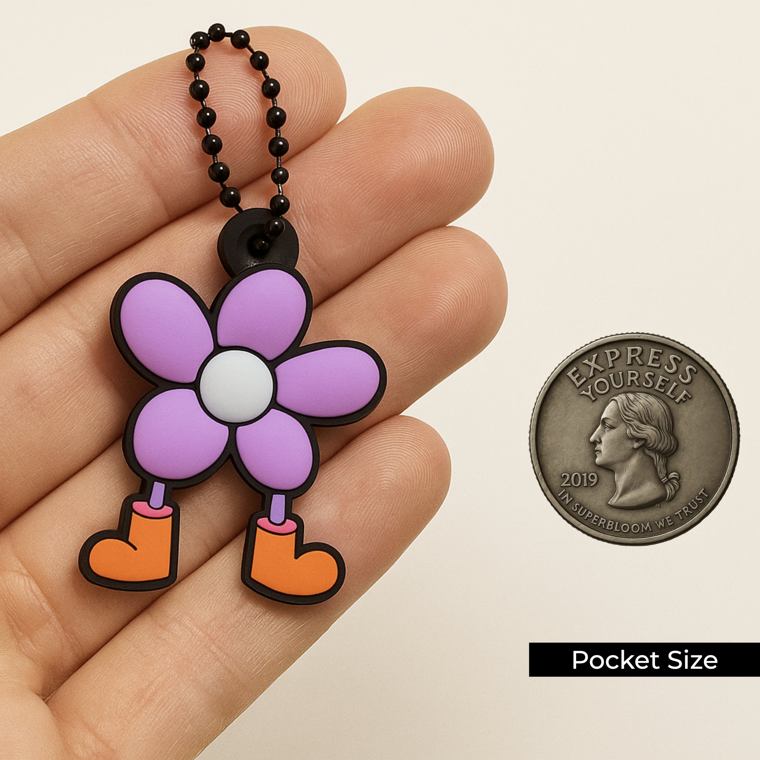 Close-up of the Dandy Bloomer flower keychain held in hand next to a size-reference coin, showing this pocket-size SUPERBLOOM charm for keys, bags, and accessories.