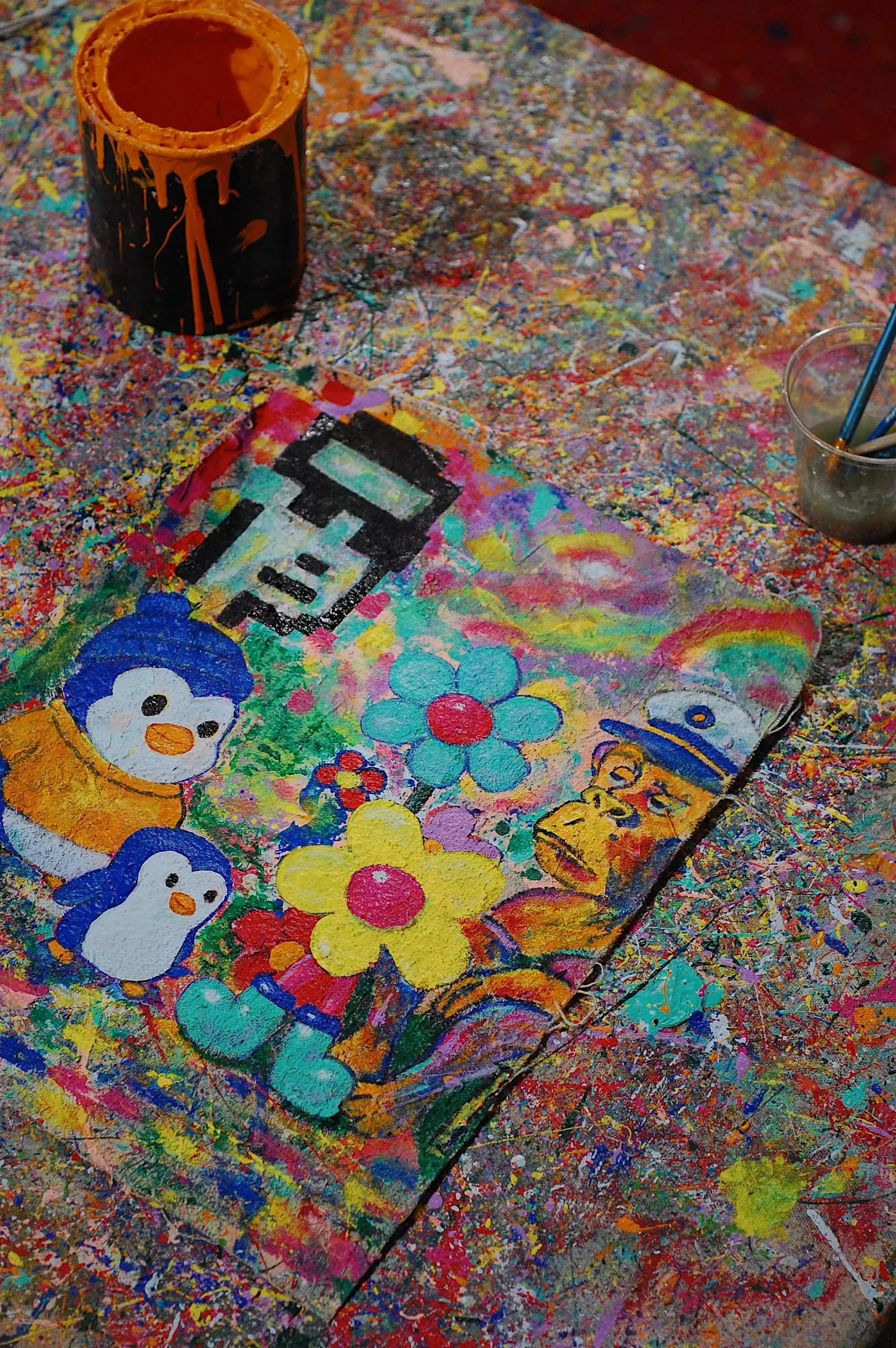 SUPERBLOOM’s Mint Your Identity painting resting on a colorful paint-splattered studio table with brushes, dripping paint can, and art tools