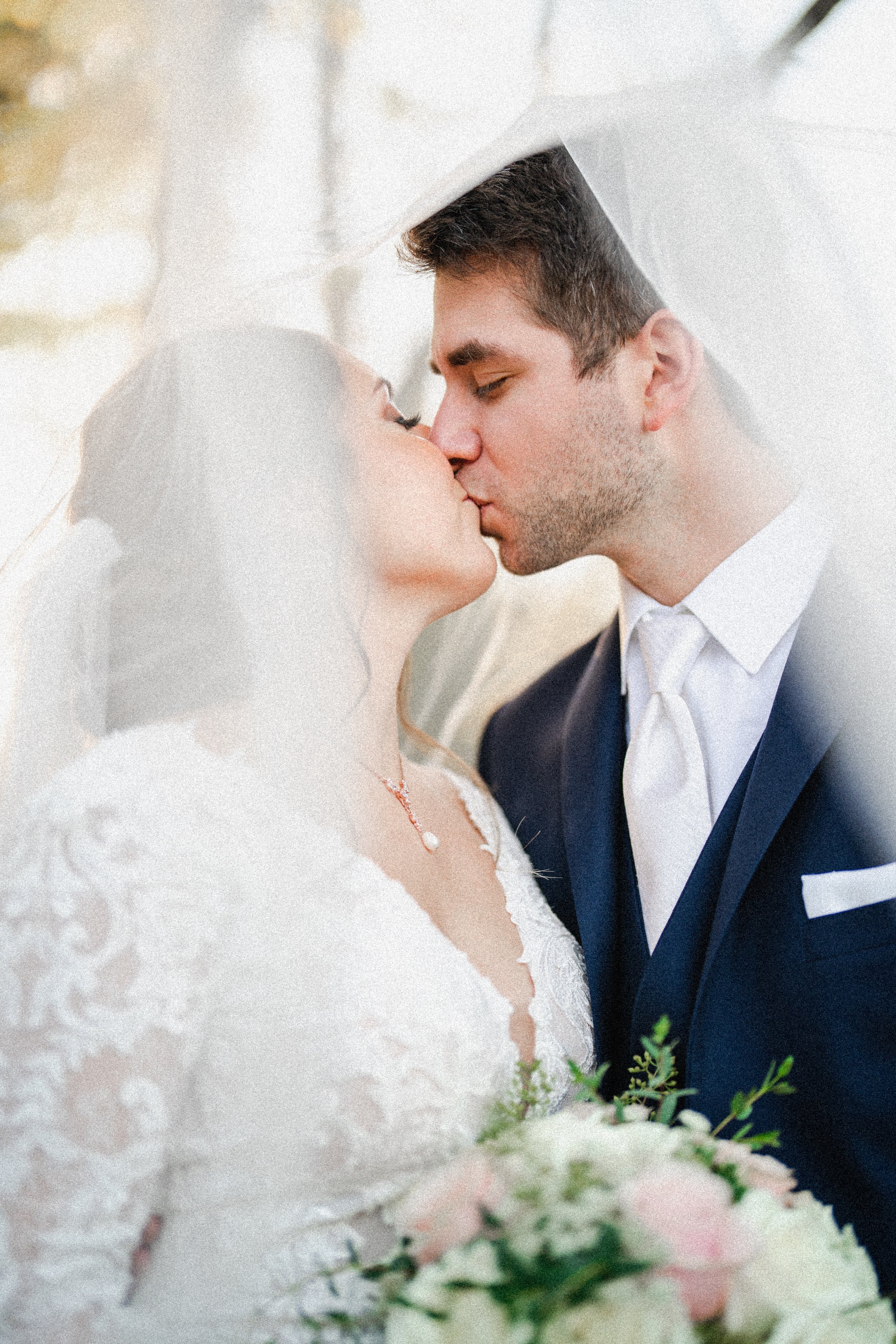 A bride and groom sharing a kiss under a veil during their wedding.