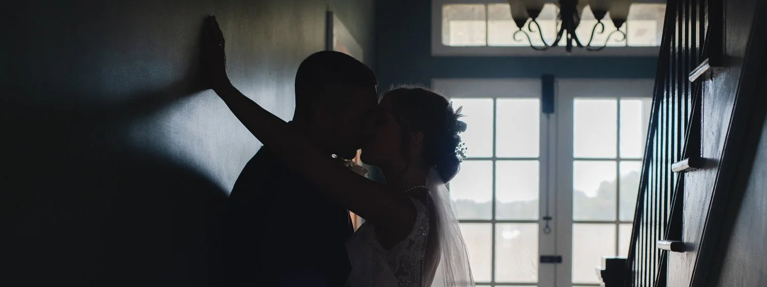Silhouette of a bride and groom kissing indoors by large windows with natural light.