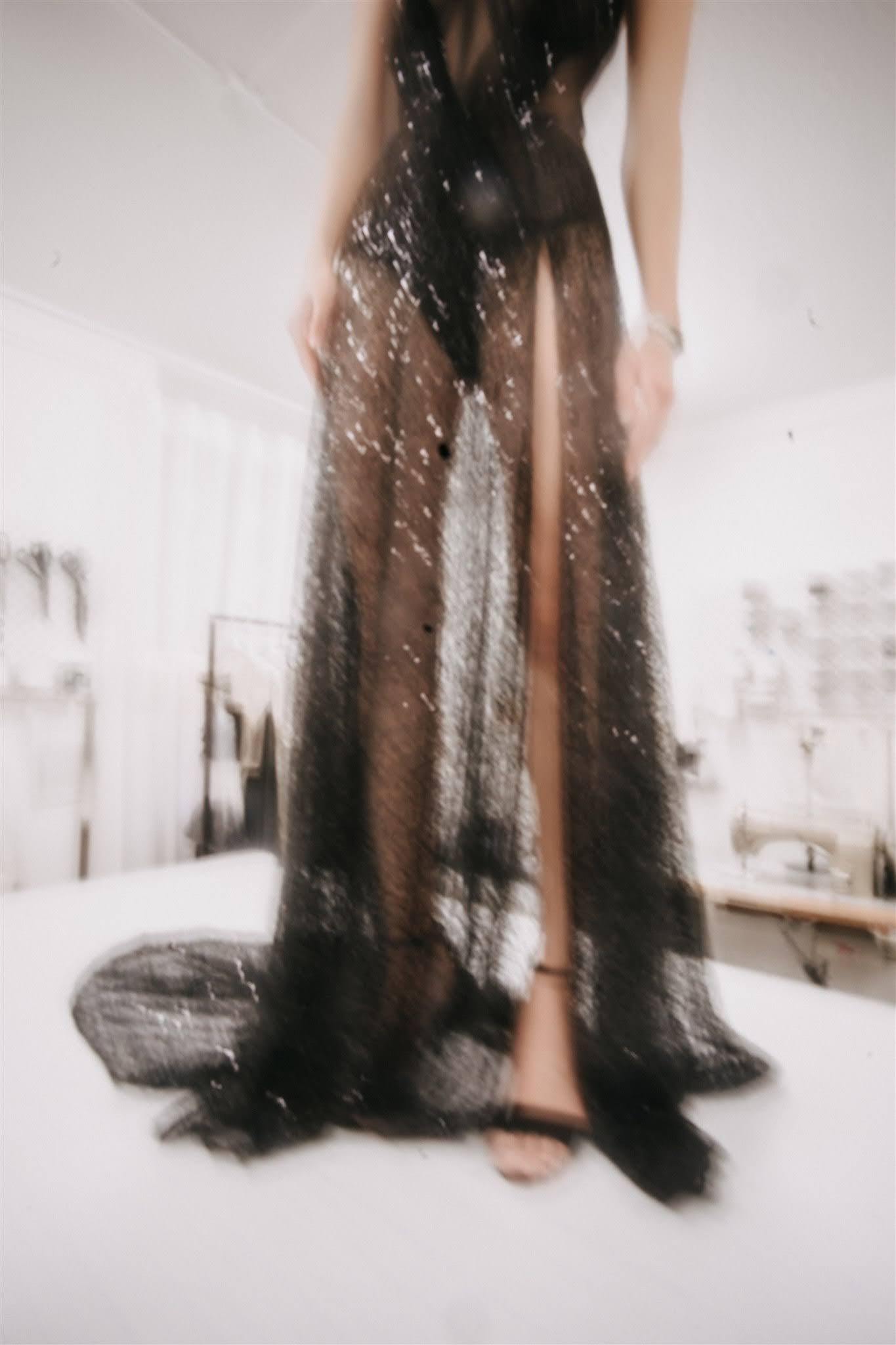 Blurred editorial image of a model wearing a black couture gown on the cutting table in the atelier