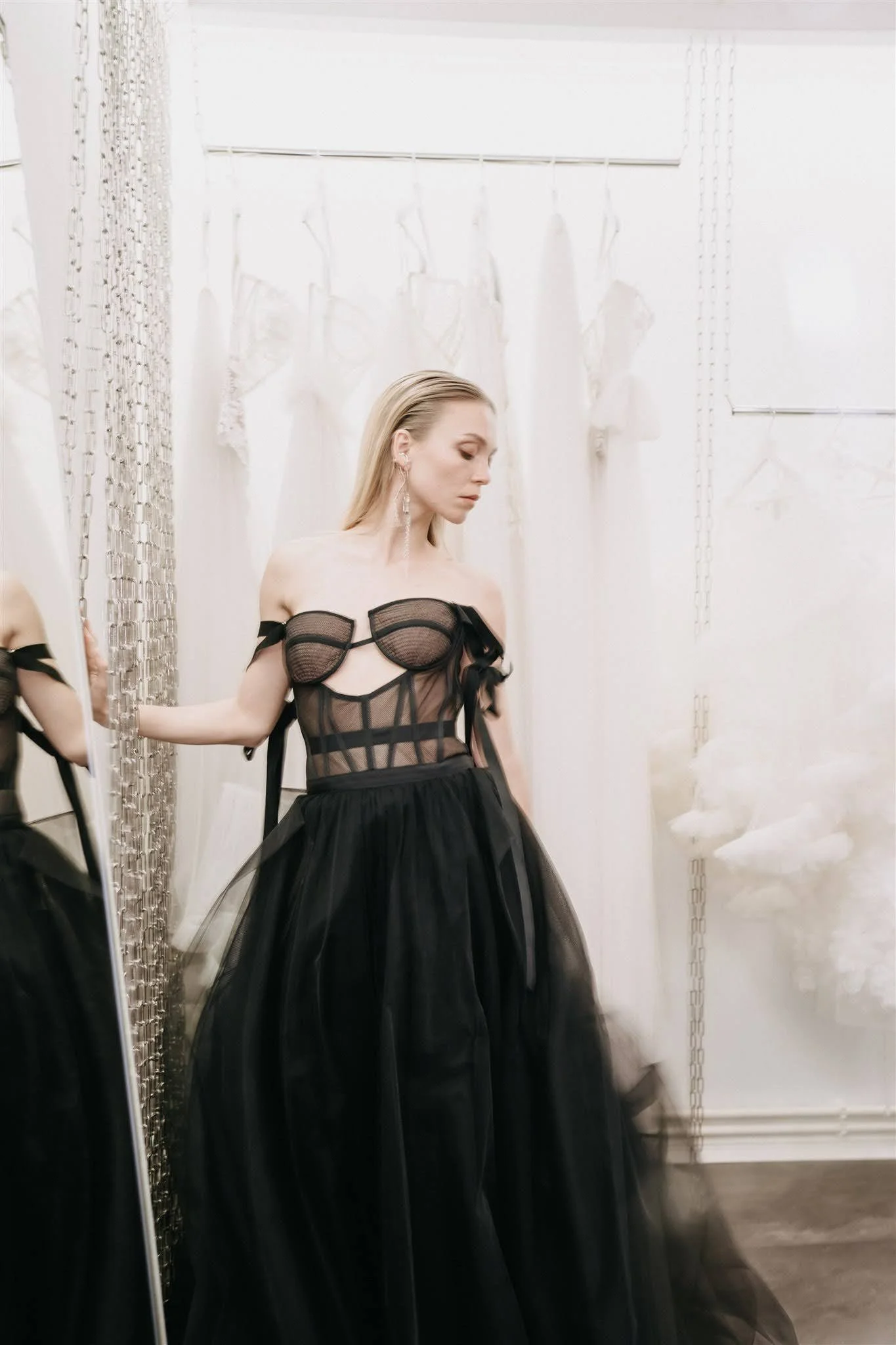 Model wearing a black couture dress posing in the showroom in front of a garment rack