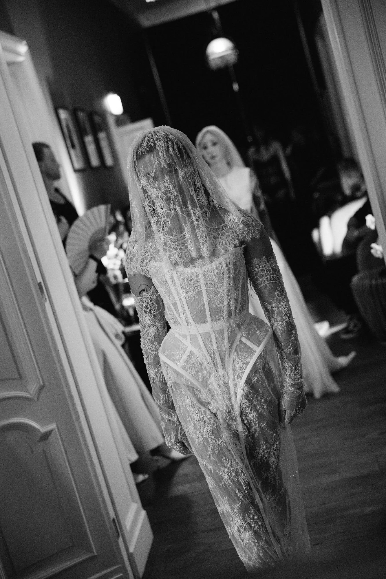 Model walking the runway wearing an edgy white lace couture dress with gloves and a veil