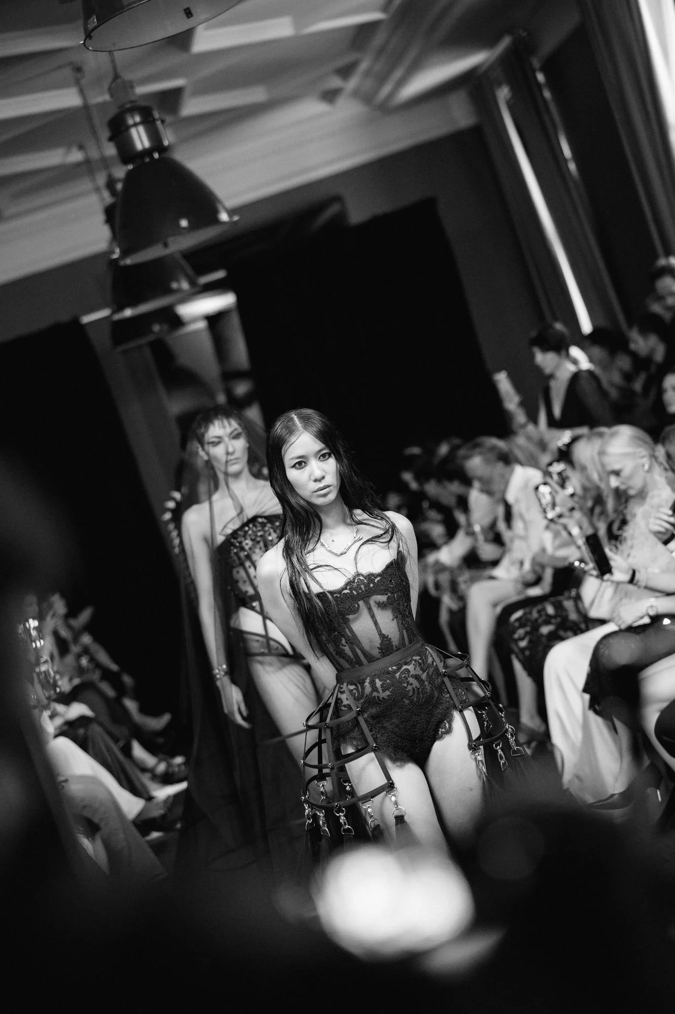 Runway finale image with a model wearing a black lace gothic-style couture gown in the foreground