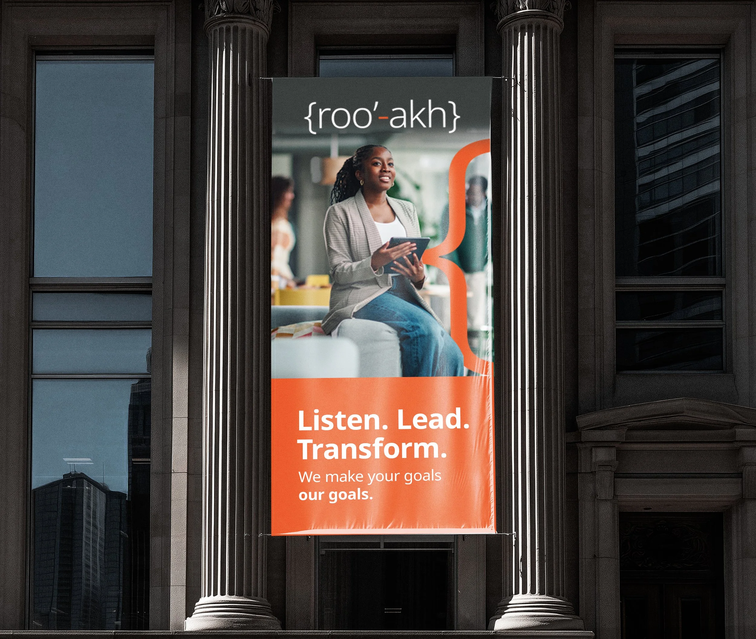Poster on a building window with a woman holding a tablet, the words '{r oo'-akh}' at the top, and the phrase 'Listen. Lead. Transform. We make your goals our goals.' at the bottom.