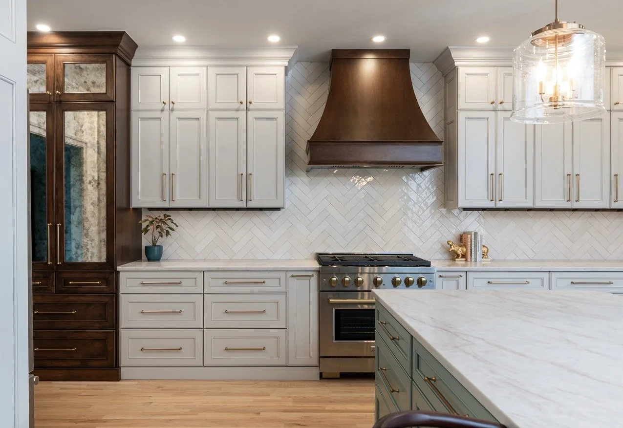 Pale gray kitchen cabinetry with wood range hood, herringbone tile backsplash, and large island in a Charlottesville kitchen renovation