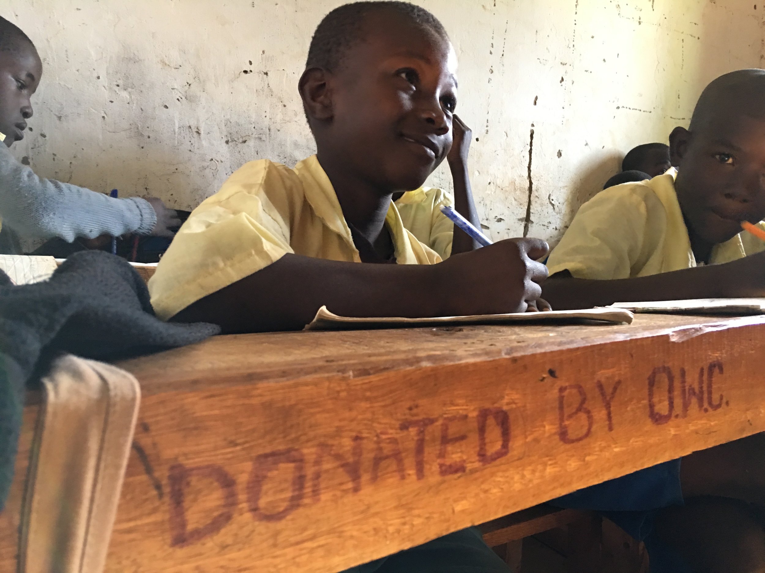 A student is seated at a desk that the OWC helped purchase during a fundraising event a few years prior. He was enjoying a lesson in math taught by one of HIP's wonderful teachers.