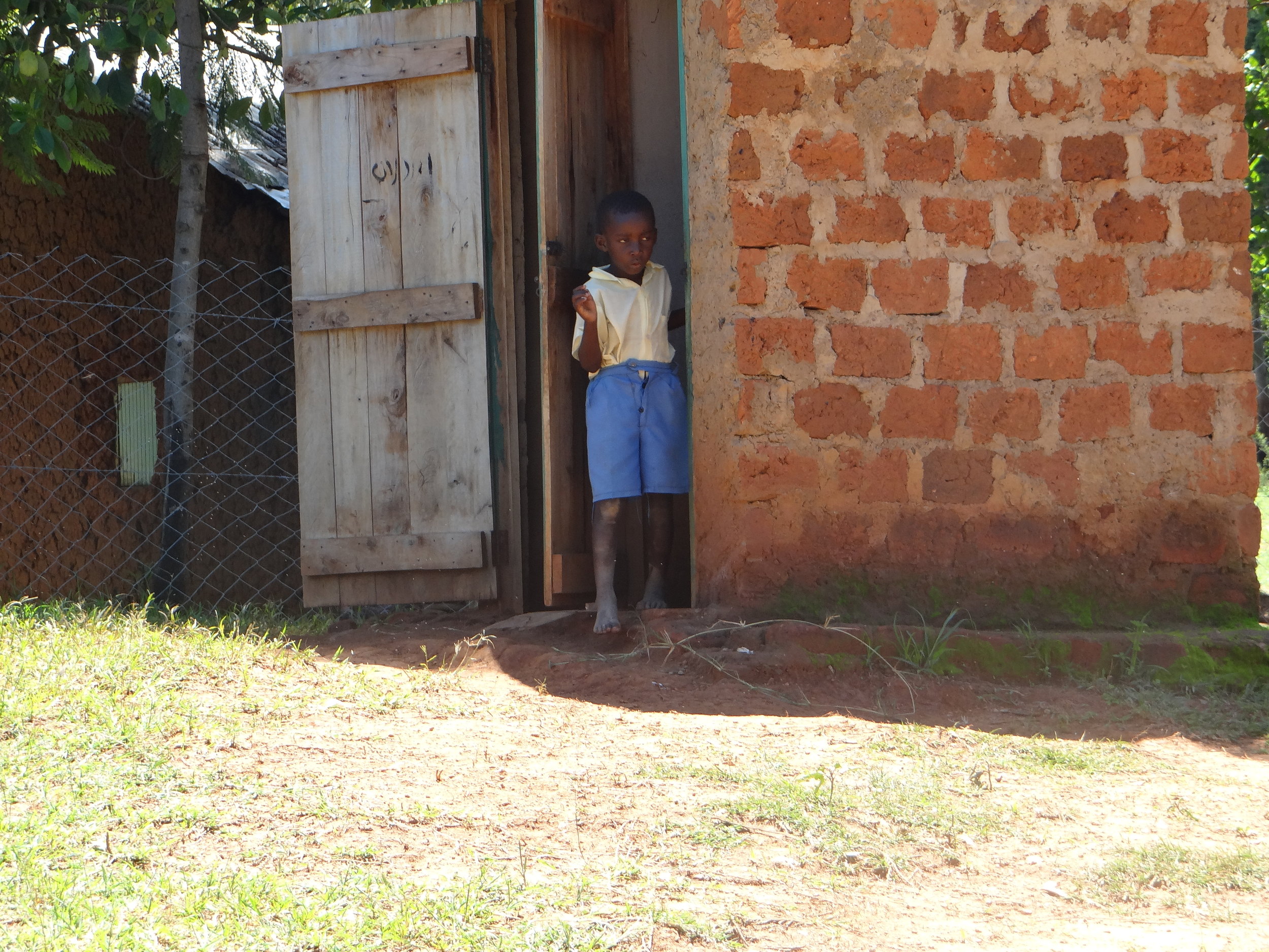 One of HIP's students coming out of the latrine. This boy did not have a pair of shoes for school.