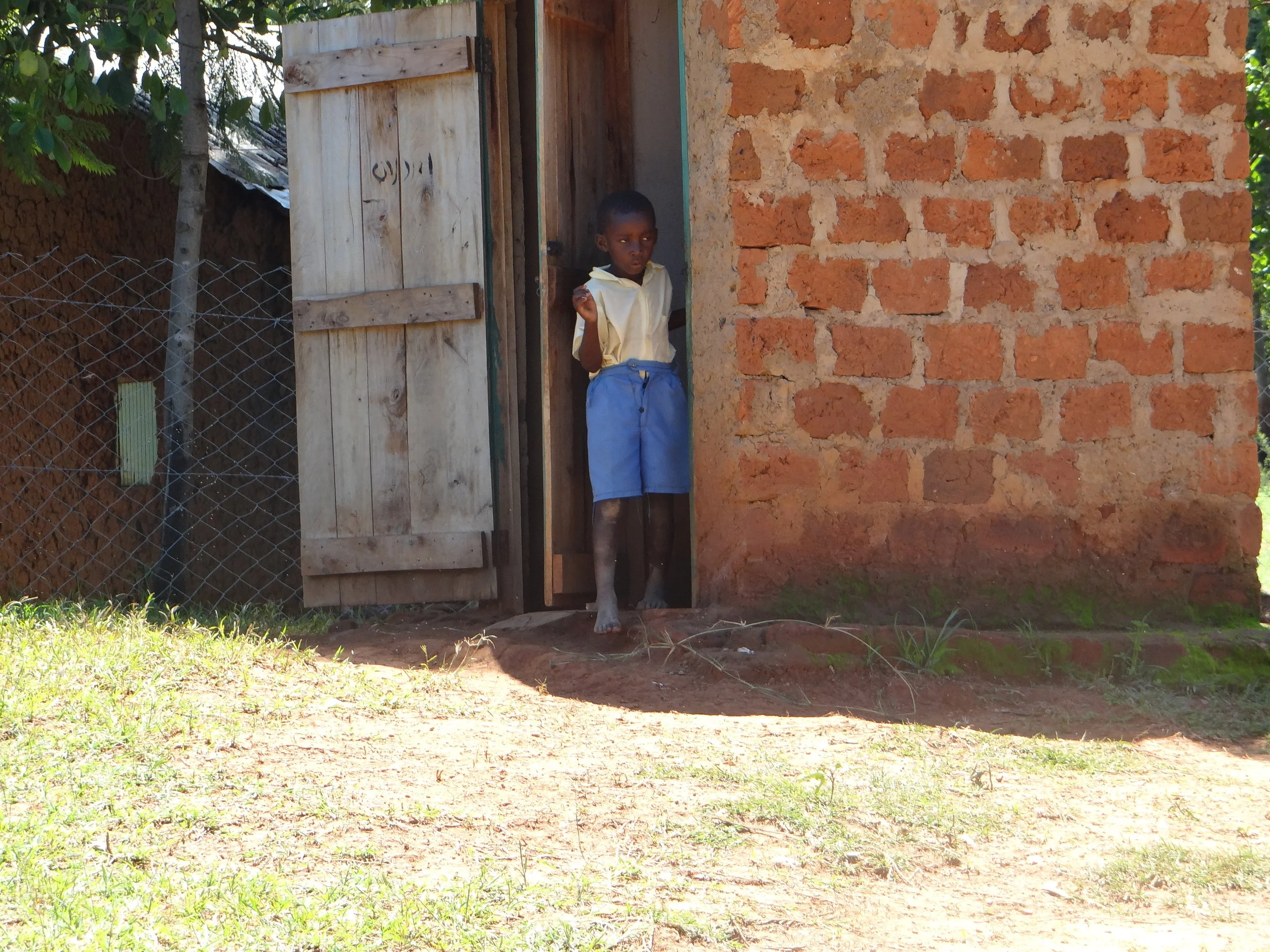 One of HIP's students coming out of the latrine. This boy did not have a pair of shoes for school.