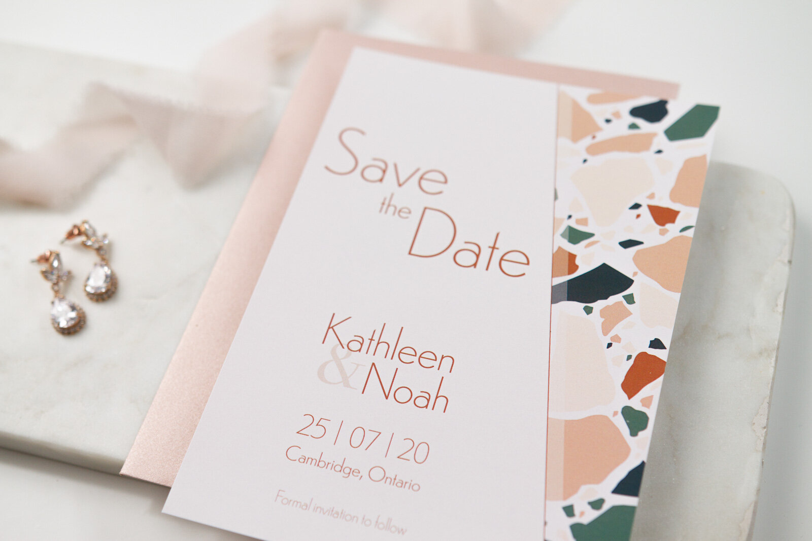 A close up of the save the date card with diagonal terrazzo tile accent and simple modern font in a deep terracotta.