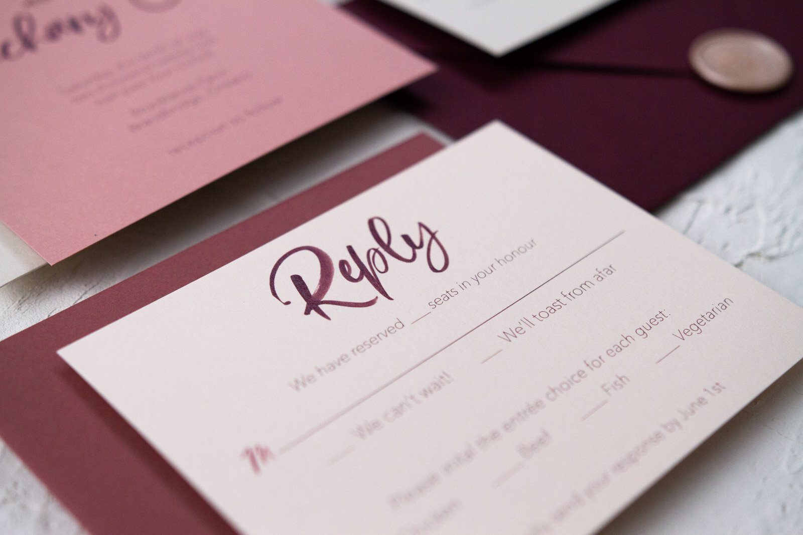  Wedding reply card on a pale pink cardstock with a modern, burgundy watercolour script.    