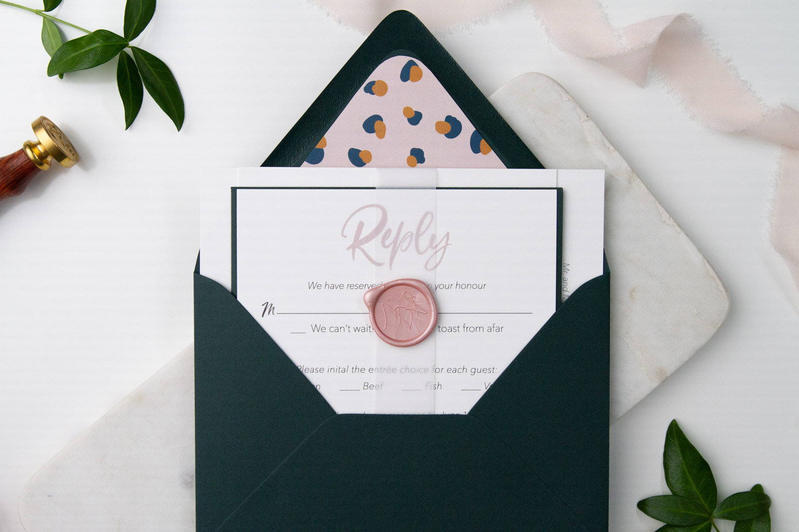  Semi-custom blush wedding invitation suite wrapped with a vellum belly band and wax seal, tucked into an emerald envelope. 