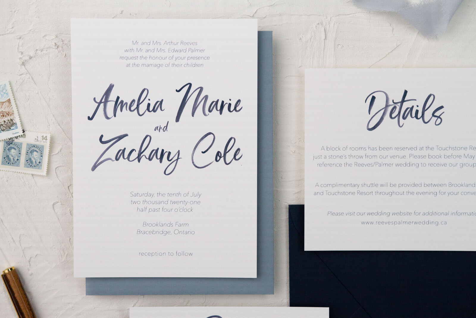  White and navy semi-custom wedding invitation and matching details card with watercolour script and dusty blue envelope. 