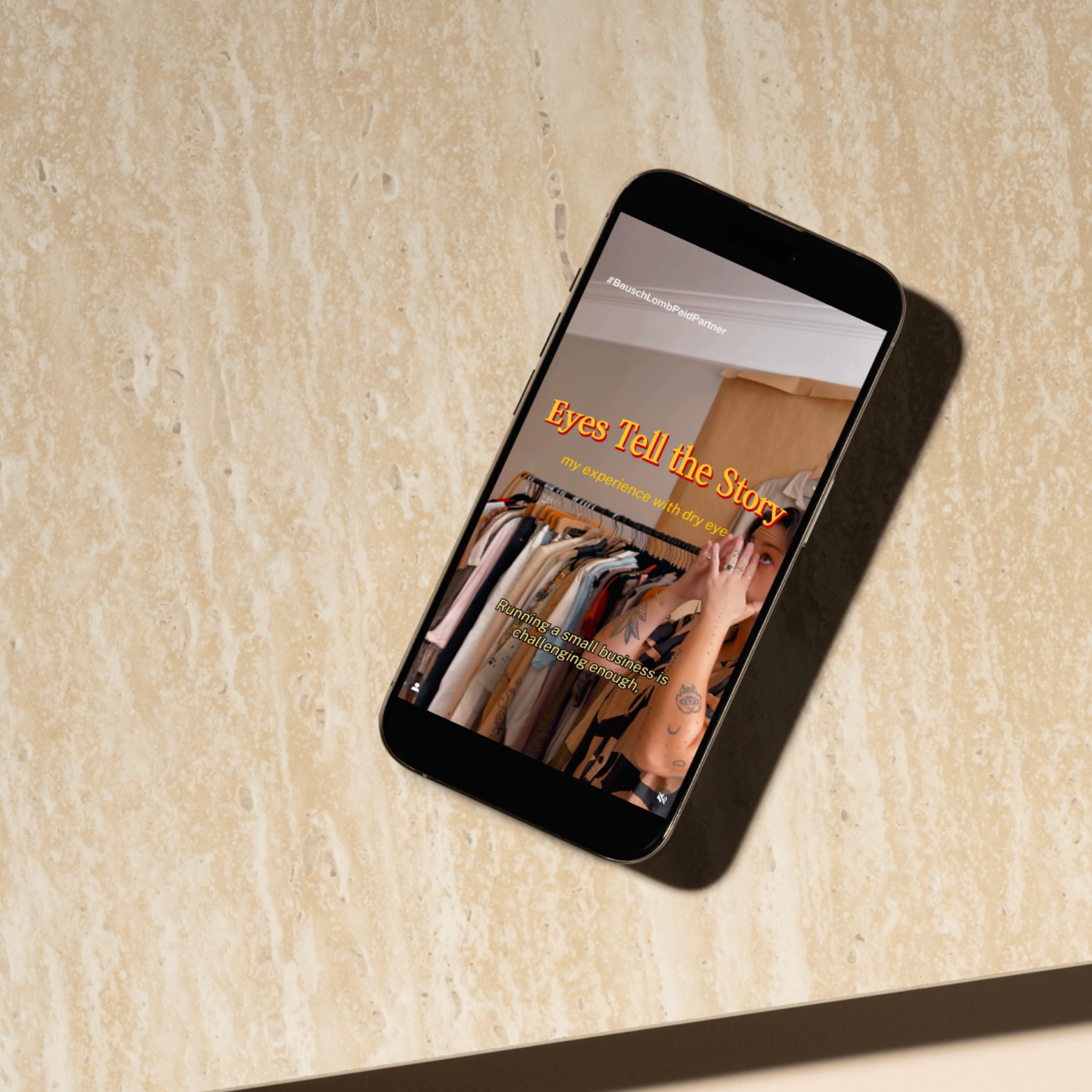 A smartphone displaying a woman with tattoos on her arm standing in front of a clothing rack filled with various garments, with an overlay of colorful text and phrases.