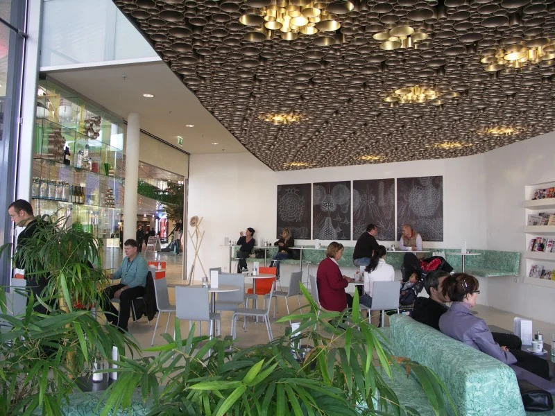 CAFE BAZAR , 2005, EUROPARK SALZBURG DORIS DOCKNER, FRANZ POLZHOFER JOHANNES BRANDSTÄTTER (ARCHITEKT UND BETREIBER) DAS CAFÉ BAZAR IM EUROPARK WIRKT, ABGESCHIRMT DURCH DEN ATMOSPHÄRENFILTER "LILITH" ALS GRÜNE "OASE" IN DER GESCHÄFTIGEN EINKAUFSMALL. EIN "FREIRAUM" FÜR "FREIDENKER" (GANZ IM SINNE DER ÖSTERREICHISCHEN KAFFEEHAUSTRADITION) WIRD MIT EINEM FLIESSENDEM, DEMOKRATISCHEN, OFFENEN RAUM UMGESETZT