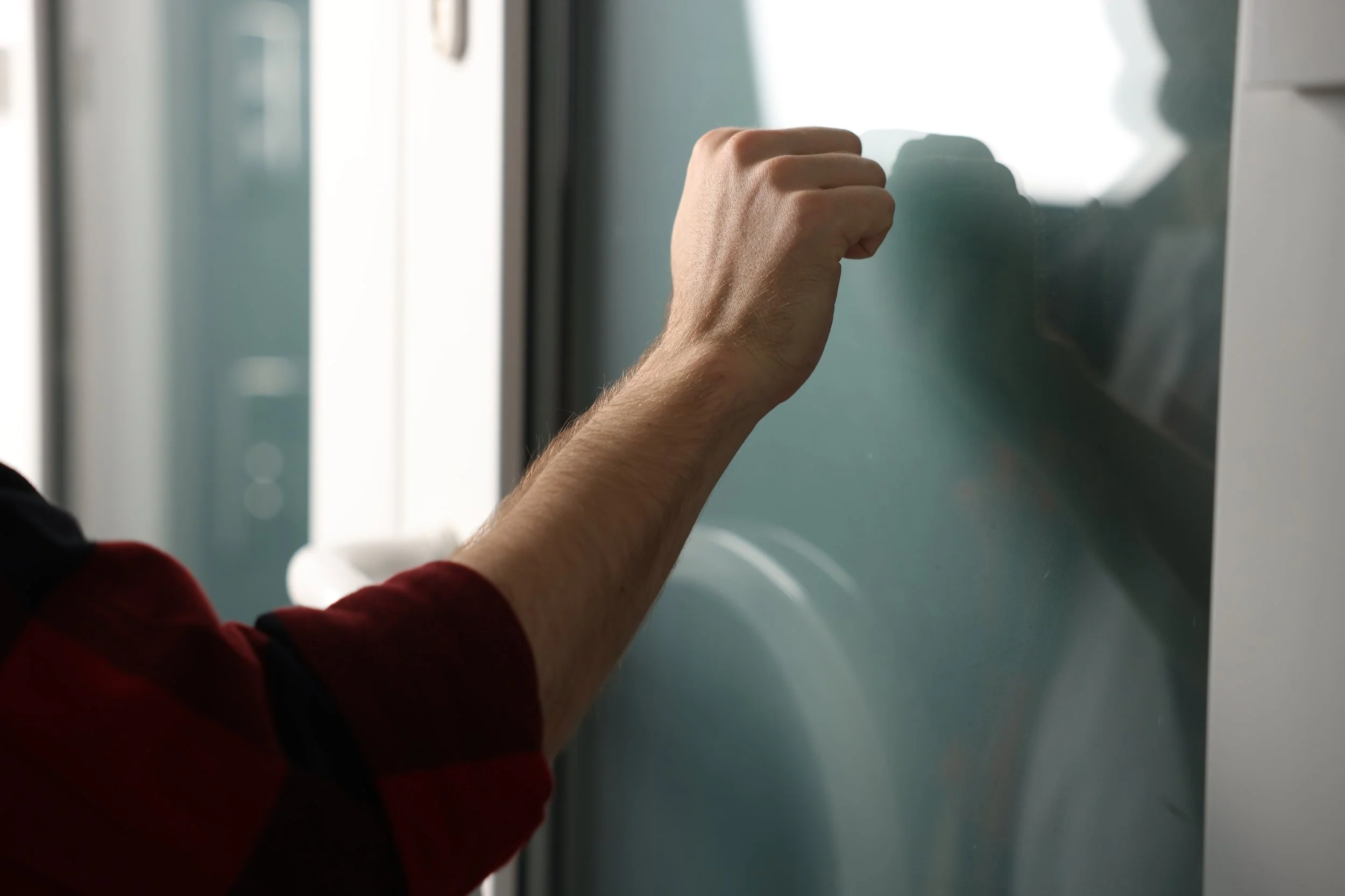 An unidentified man wearing a red shirt knocks on a glass door.