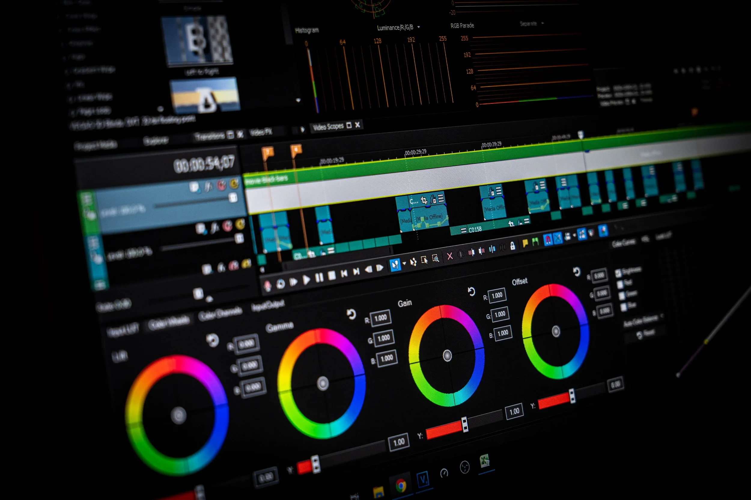 Close-up of a computer monitor displaying photo editing or color grading software with color wheels, video clip timeline, and various control panels visible.