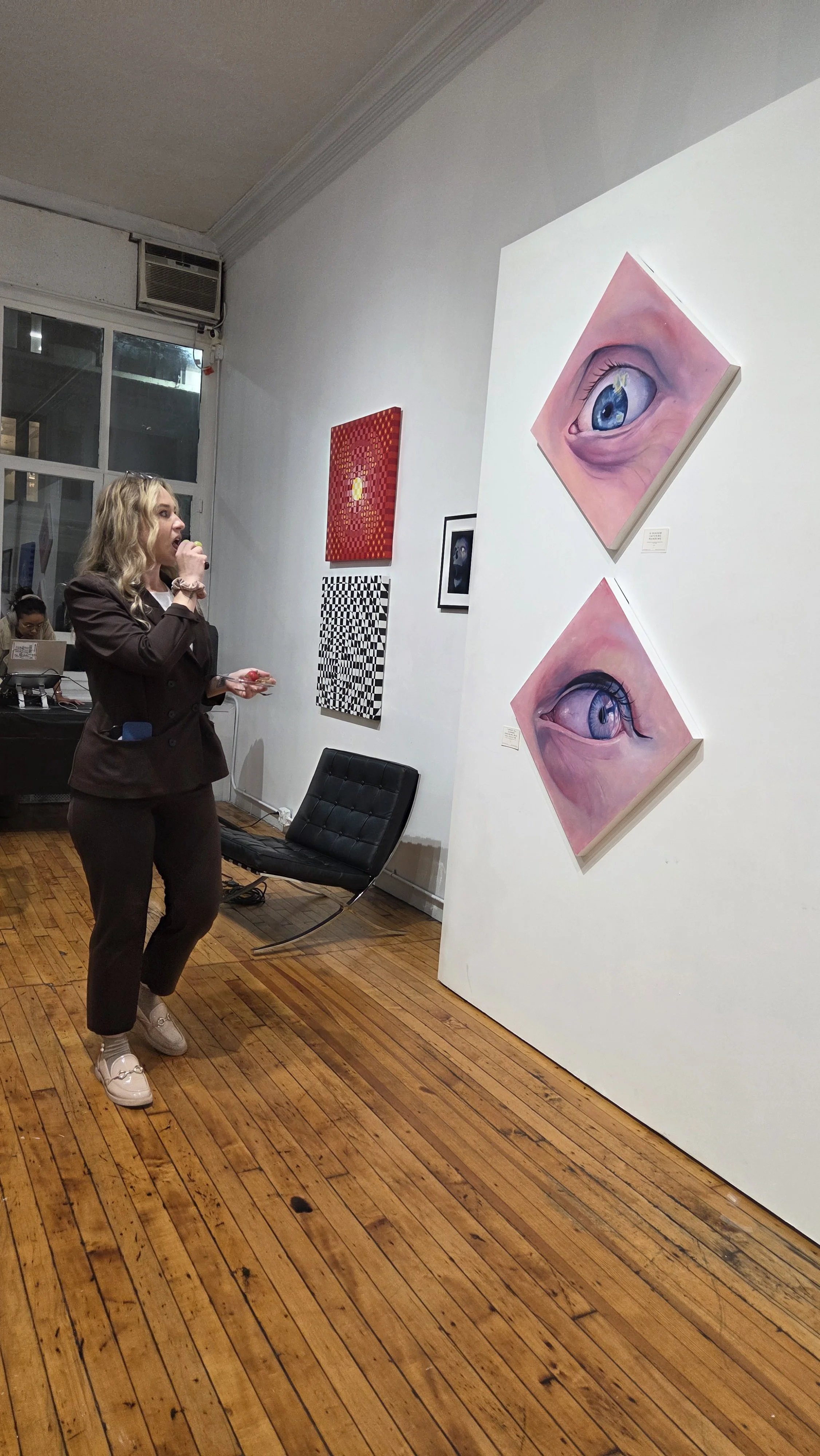 A woman standing in an art gallery with paintings of eyes on the wall.
