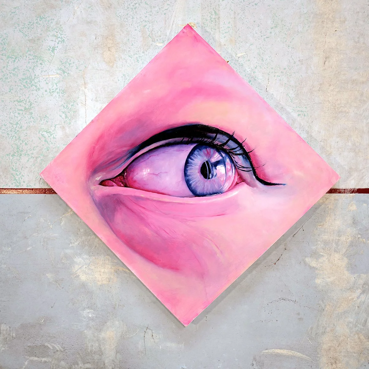 A painting of a human eye on a pink background, displayed lying diagonally on a textured surface.
