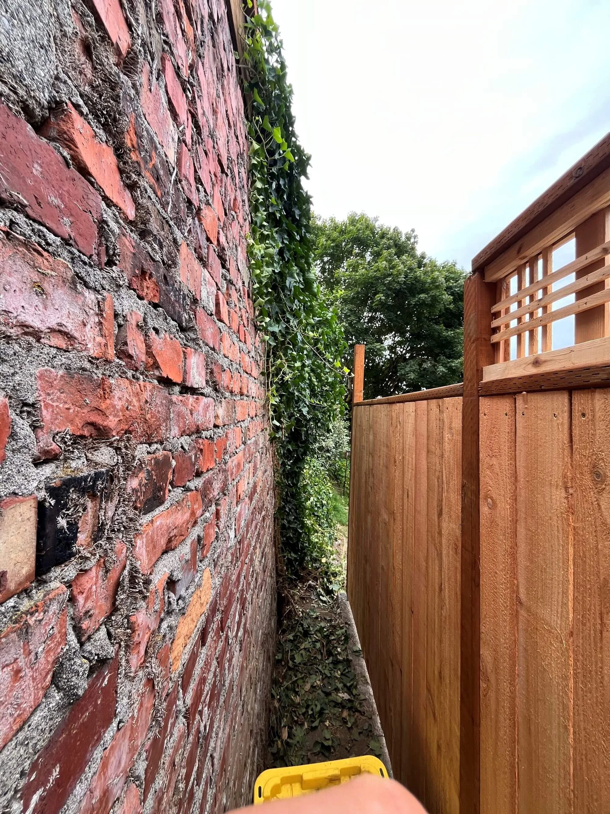 New cedar fence installation against a brick wall. At Gold Mountain Contracting, we can adapt to your existing spaces.