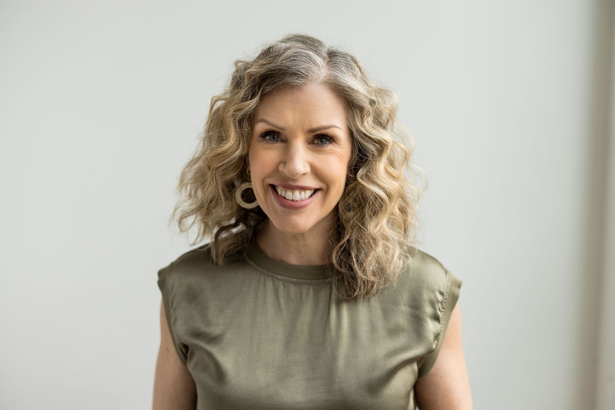 Dana Van Nest smiling in as shiny olive sleeveless blouse.jpg