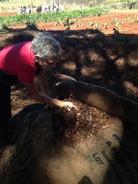 Mindy uncovering the burlap bags to show the food waste layered between wood chips.