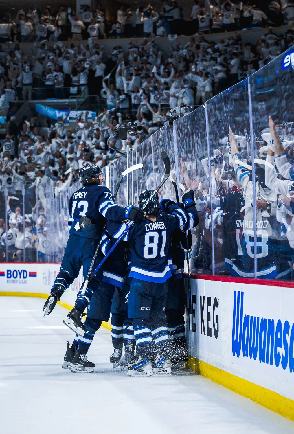 Ice hockey players celebrating near the boards during a game with a crowd of fans cheering in the background.