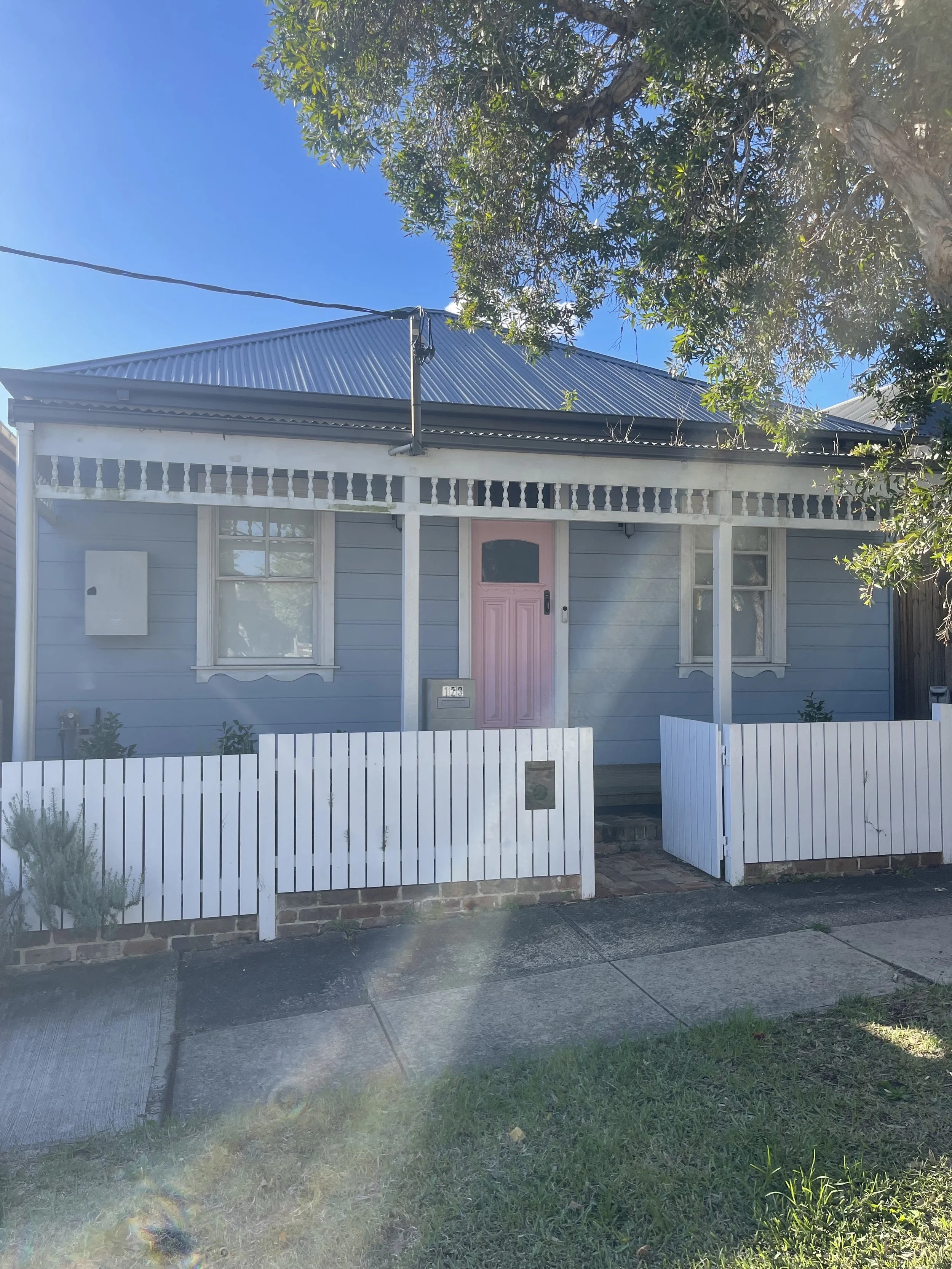 A light blue house with a pink front door, white trim, and a white picket fence, situated in Ashfield