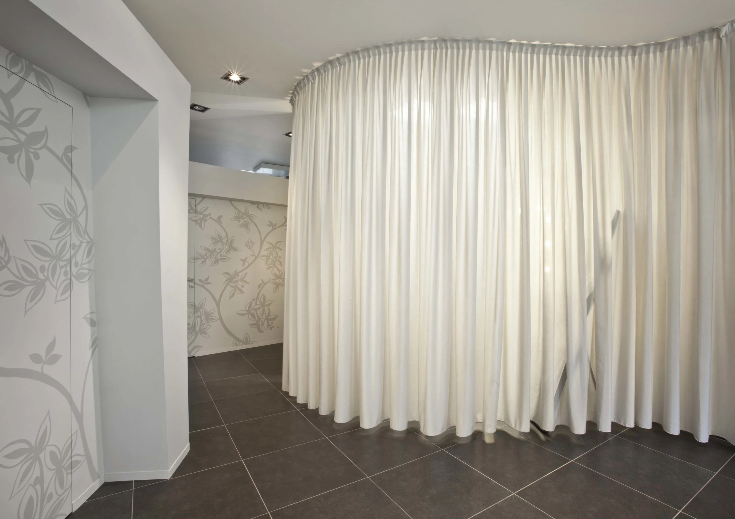  La quinta di tessuto si sviluppa verso il centro della sala in un movimento morbido delimitando la postazione per il trucco, trasformando la tenda in una grande lampada che conferisce al locale un'illuminazione morbida esaltando la palette dei color