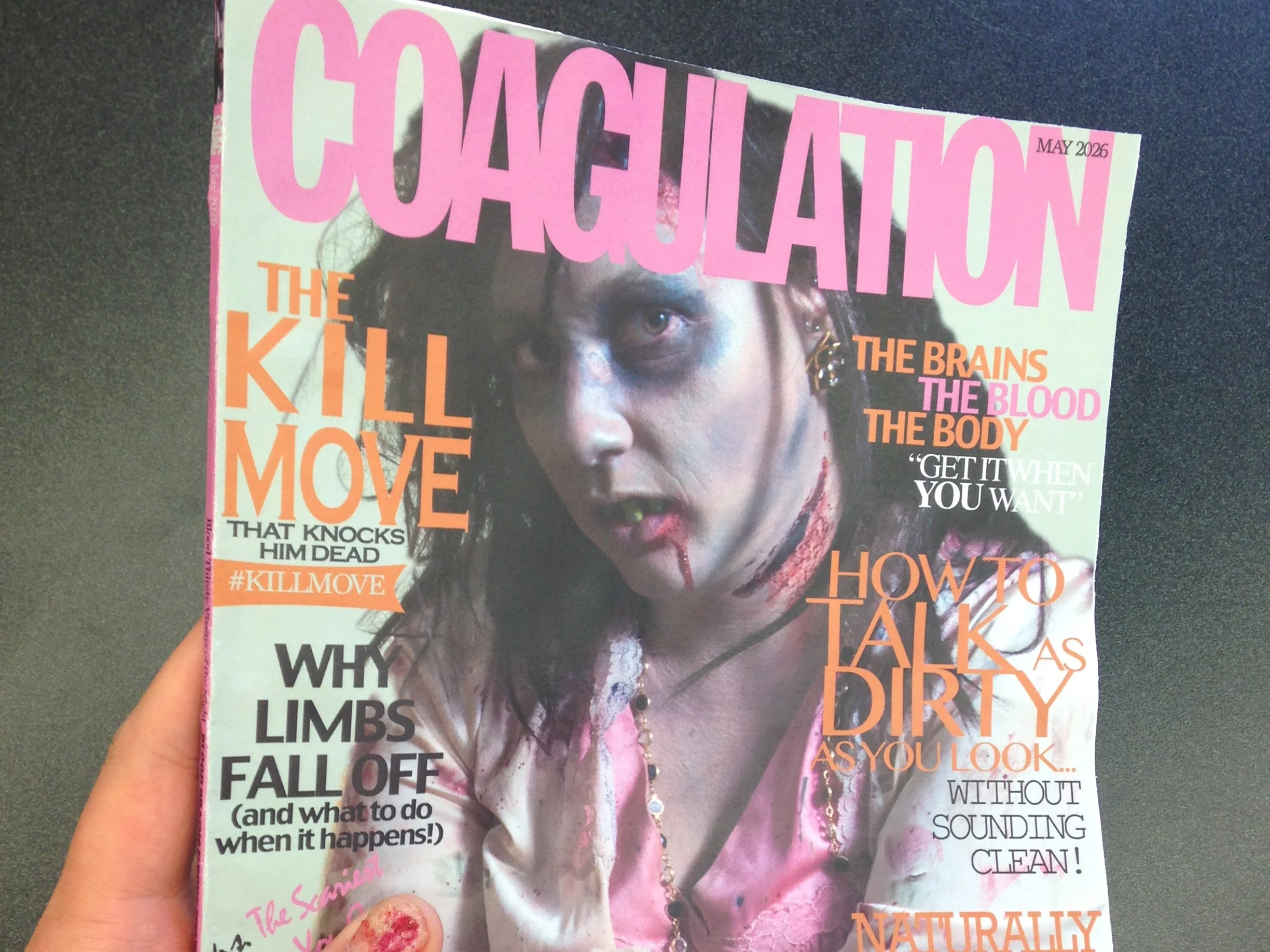 Close-up of a magazine cover featuring a woman with dark hair and makeup, with numerous headlines in bright pink, orange, and black text overlapping. The magazine issue is May 2026.