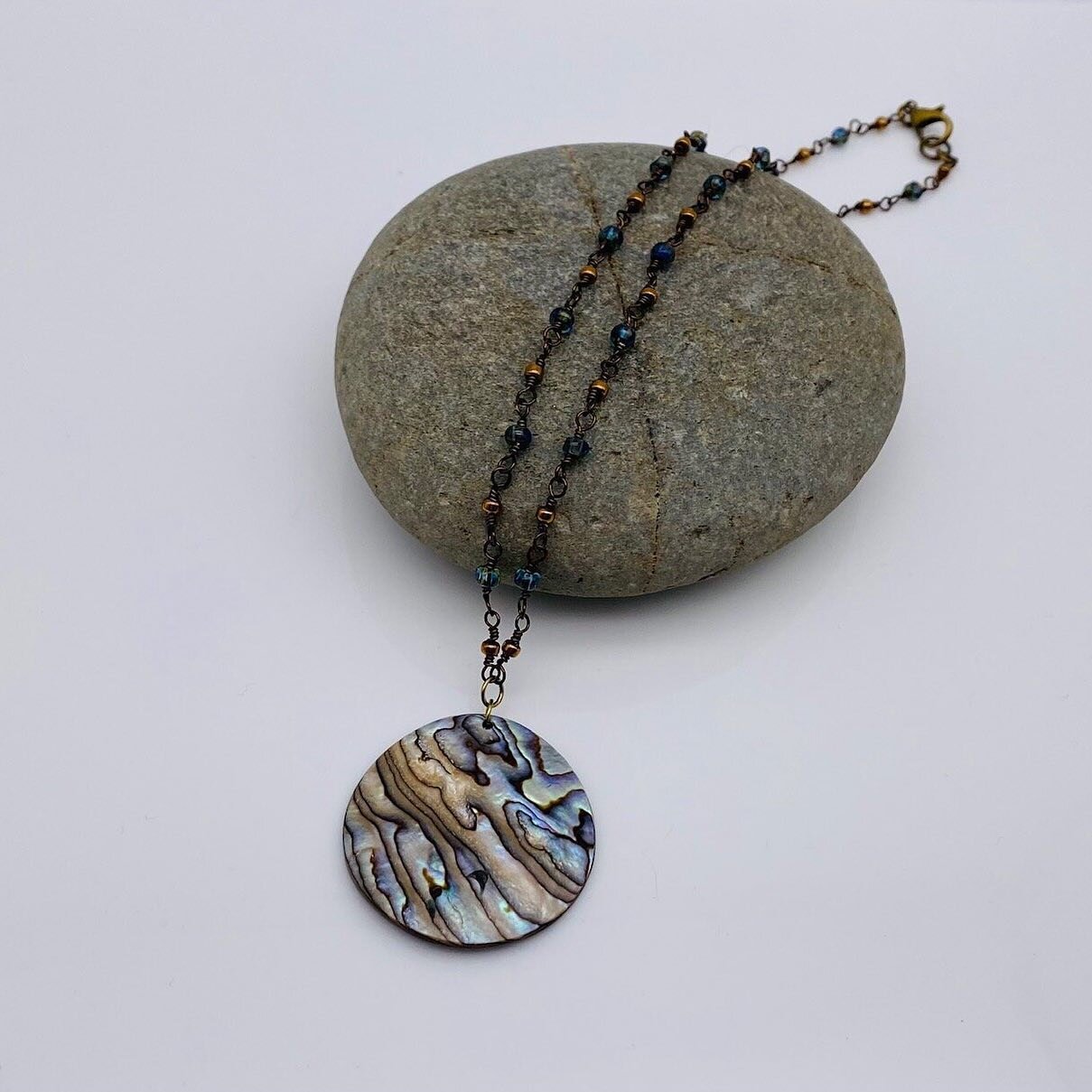 Often used in metaphysics to provide tranquility by serving as a guardian of the heart, abalone shell seeks to remind us of the inner strength we all possess.

Made from bronze plated copper, an abalone shell focal reminiscent of waves hangs from a d