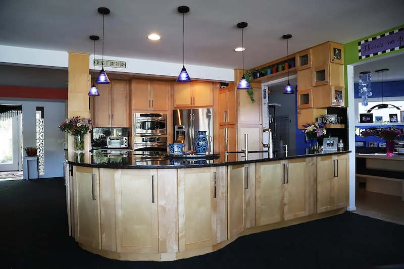 A very large work surface with lots of storage below on both sides. A supporting pole houses spices. The floating cabinets on the right house dinnerware, glasses, and display-even over pass-through. Pendant lights keep it airy!