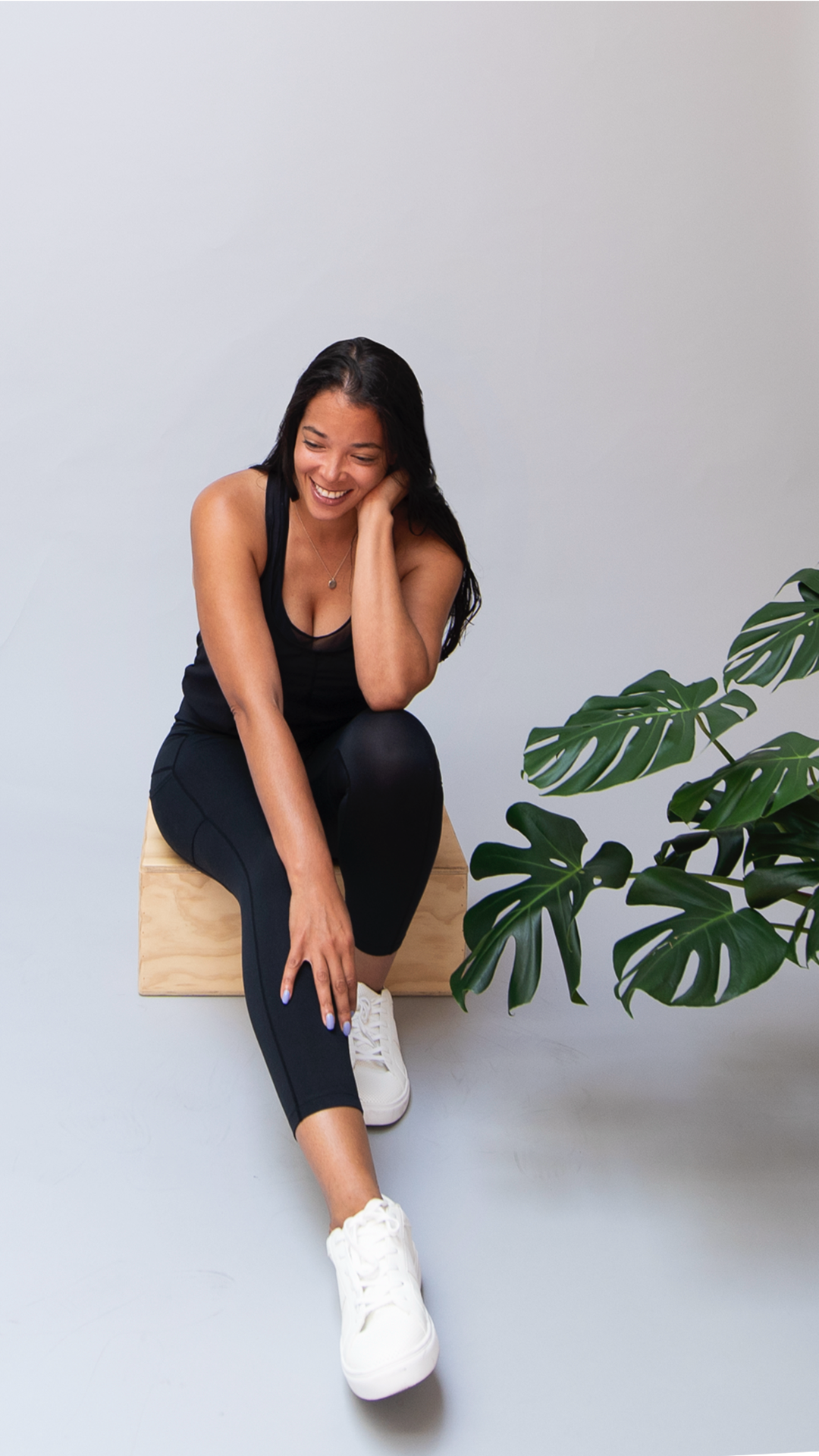 Picture of Carmen Scott sitting down looking off camera down toward the floor with a monstera plant near by on left side of Carmen.