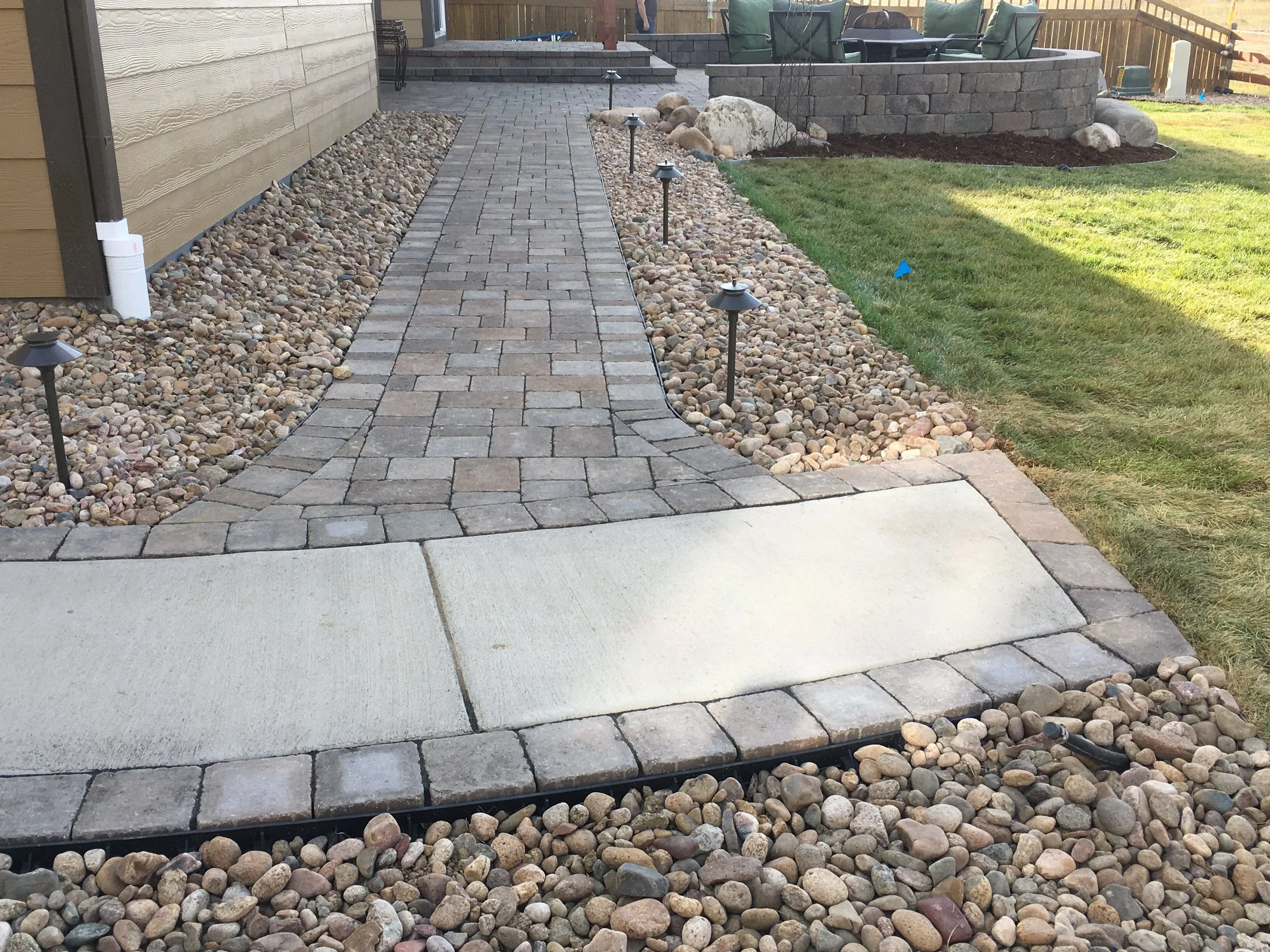 Paver, river rock, and concrete walkway along outdoor edge of home