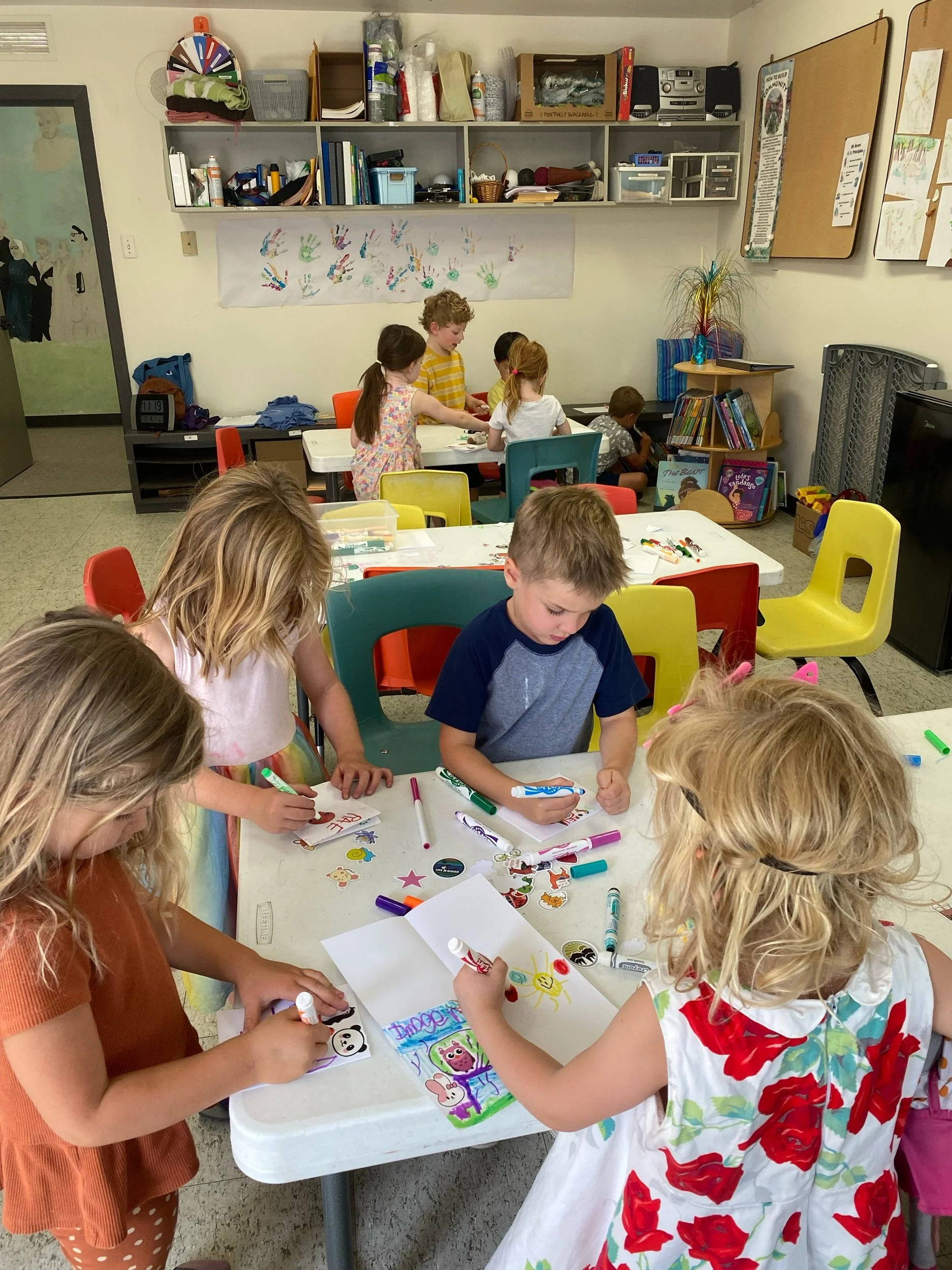 four children in a circle at a table drawing with markers on paper