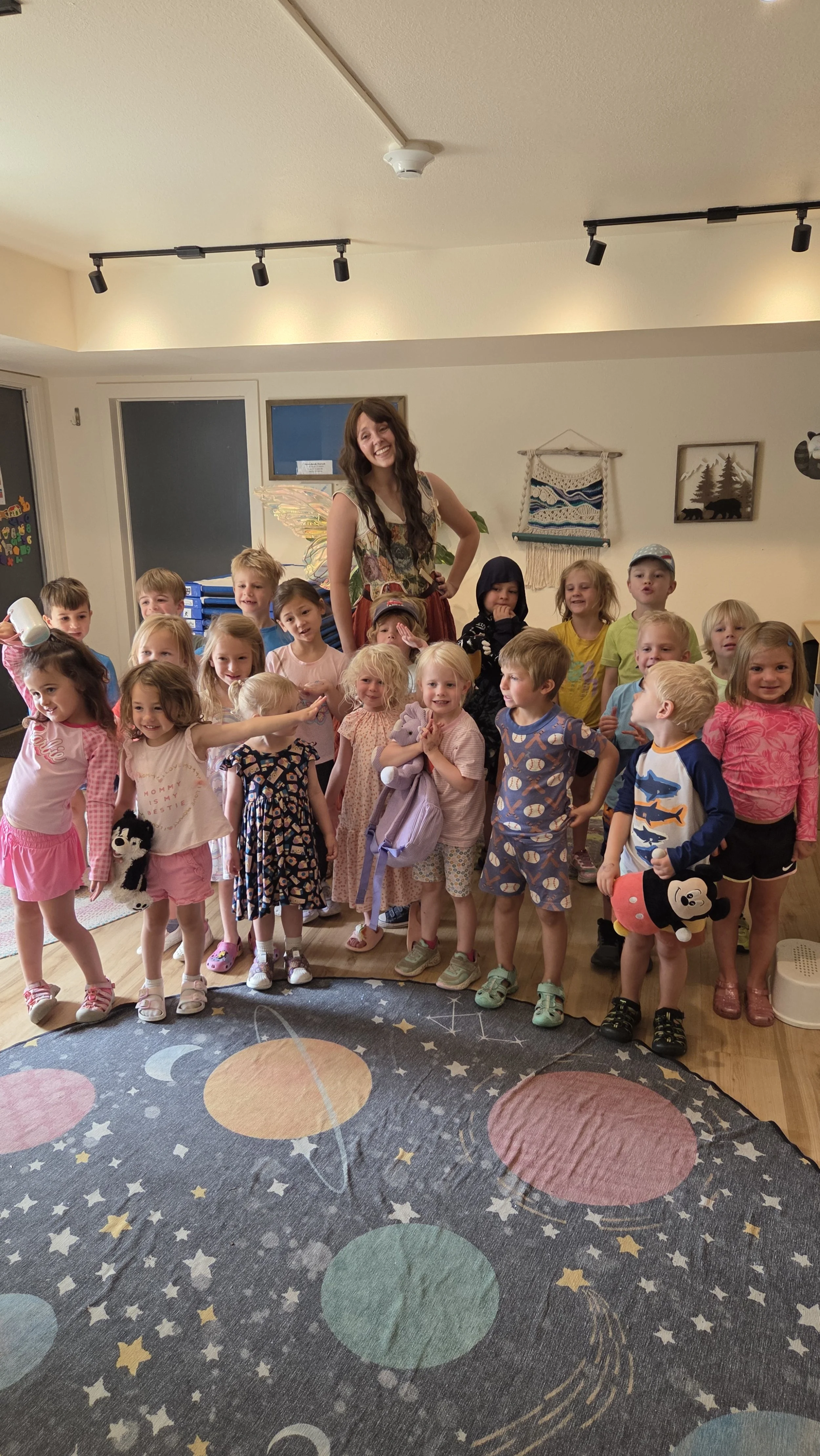 A group of young children and a woman in costume with fairy wings posing in a decorated room.