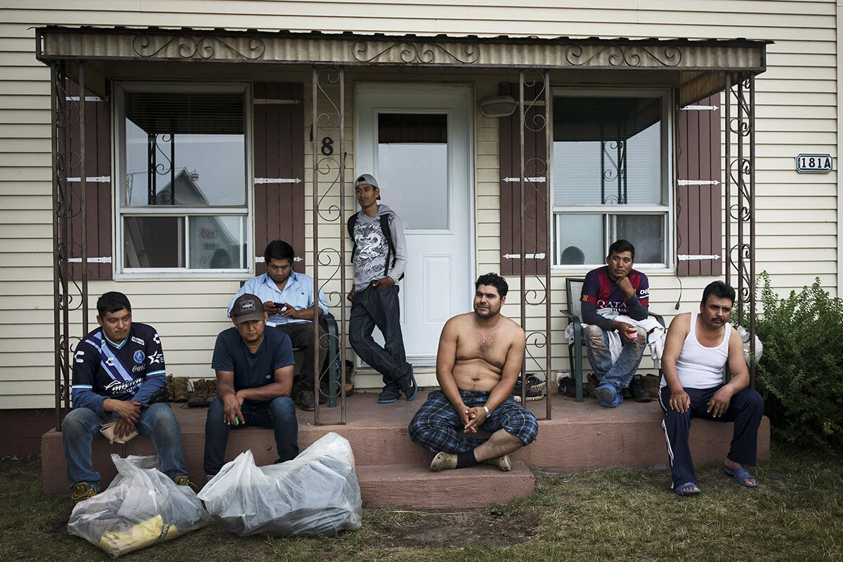 A group of Mexican migrant workers sit on the front porch of a house in Lavaltrie, Quebec, after finishing their work on a nearby farm. Some 97 per cent of workers participating in SAWP are men. As a result of complaints filed by the United Food and Commercial Workers union, Mexico stopped allowing employers in Canada to request workers of a specific gender in 2016.