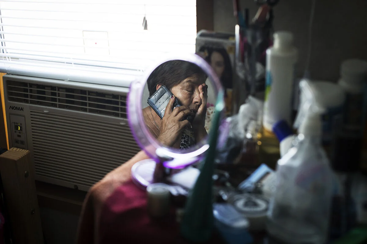 Isla calls home to her family in Mexico from her tiny, shared bedroom in Ontario and learns that her elderly mother has fallen and injured her shoulder. Distressed that she is not there to help, she bows her head in grief.