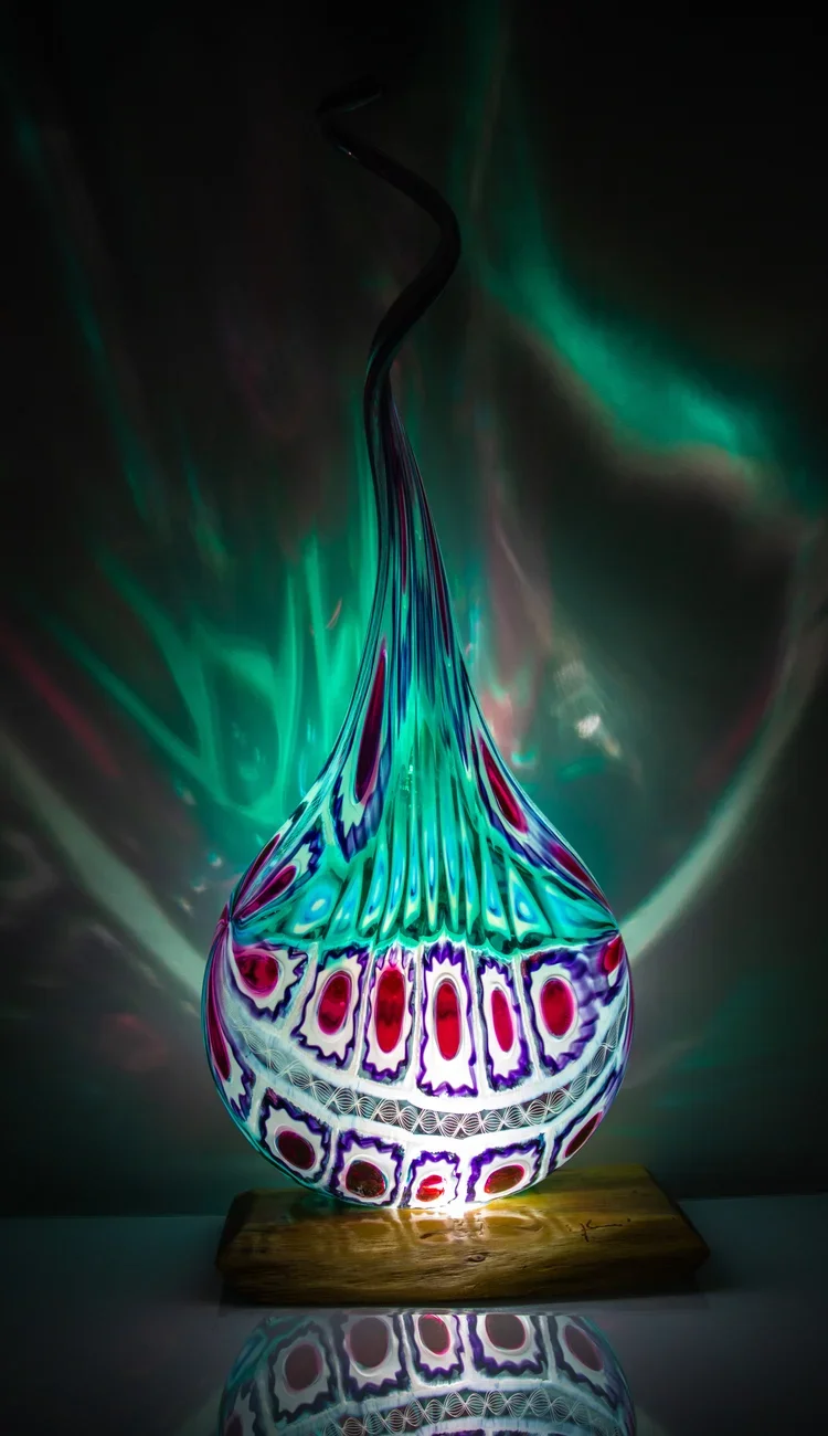 Illuminated murrini blown glass sculpture by Randy Schaffer in teal, red, and purple on a hardwood light base, projecting colorful reflections