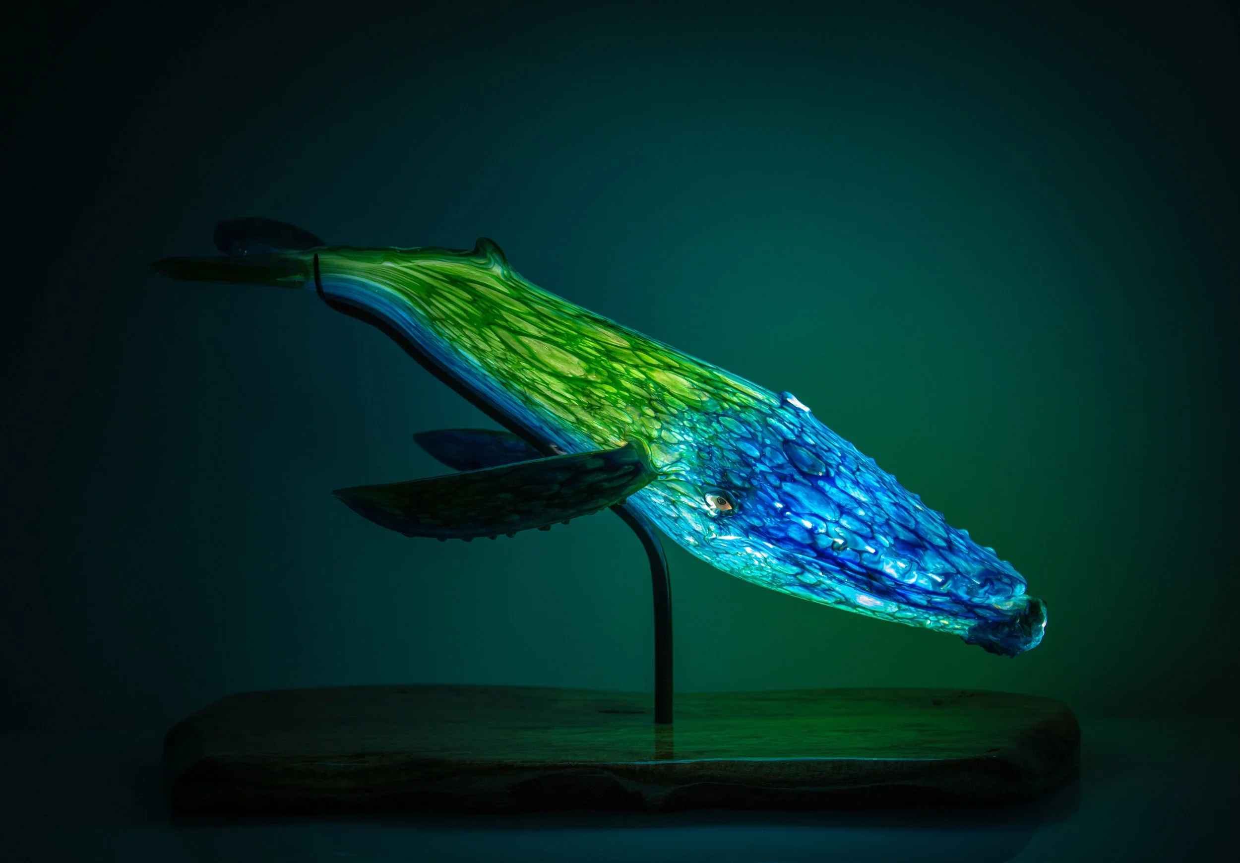 Blown glass humpback whale sculpture in blue and green on a hardwood base, handcrafted by Justin Brown at Makai Glass Maui