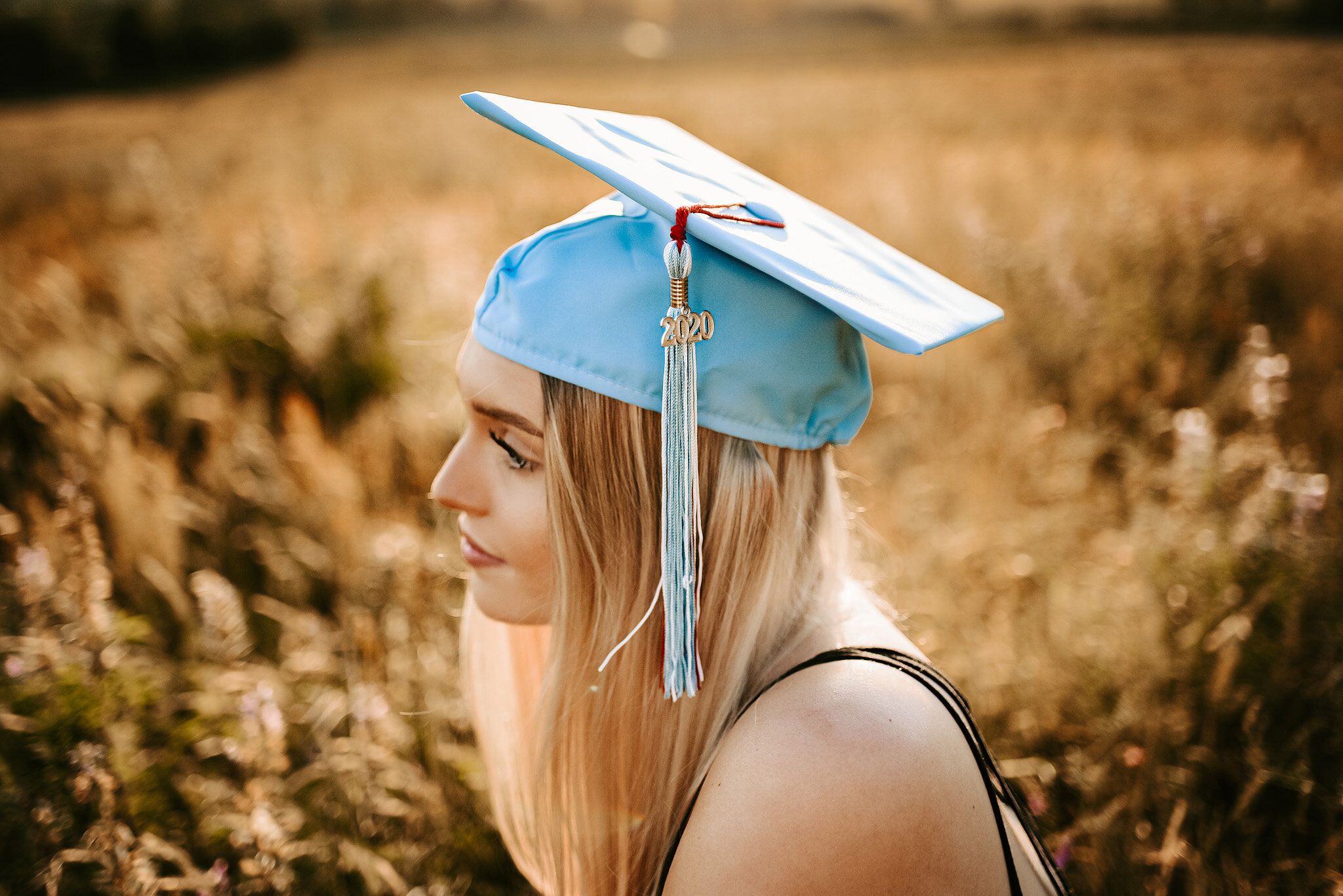 Senior girl with blue graduation cap in brown field