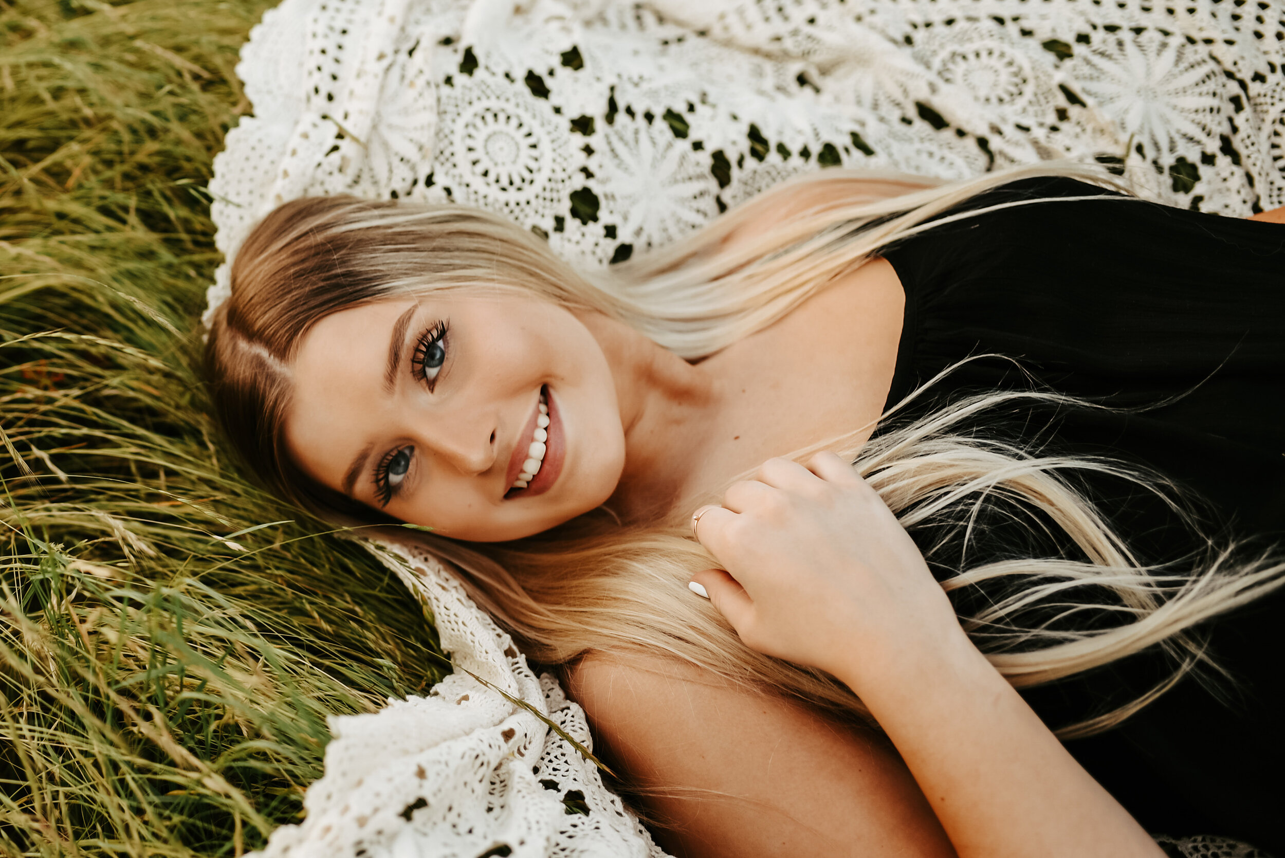 Senior girl laying on lace blanket smiling at photographer