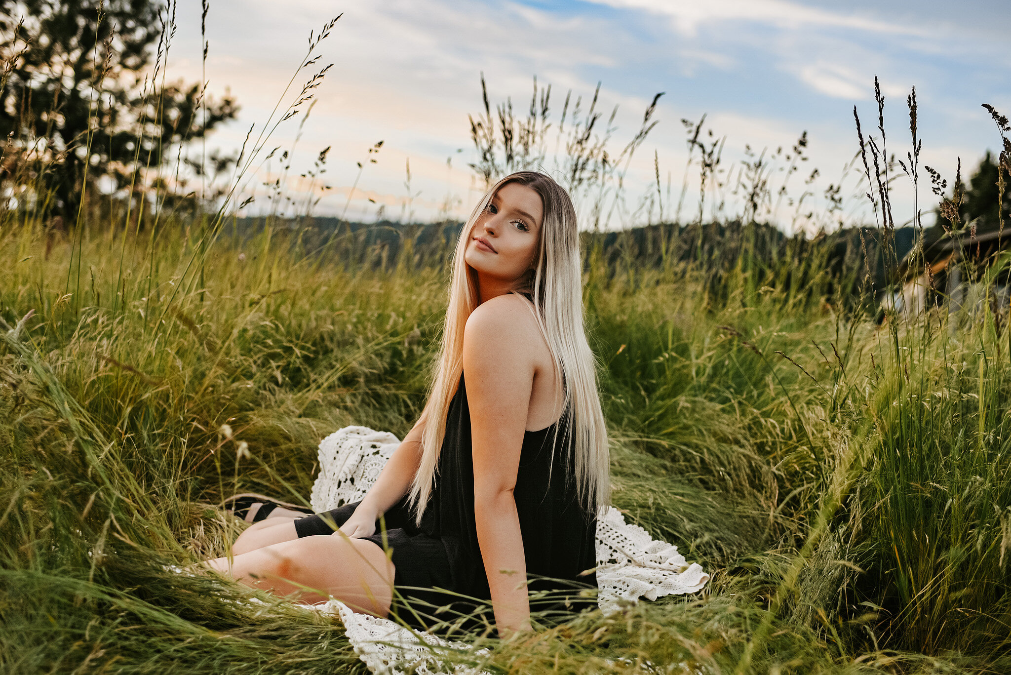 Senior girl in field, sitting down on blanket looking at photographer